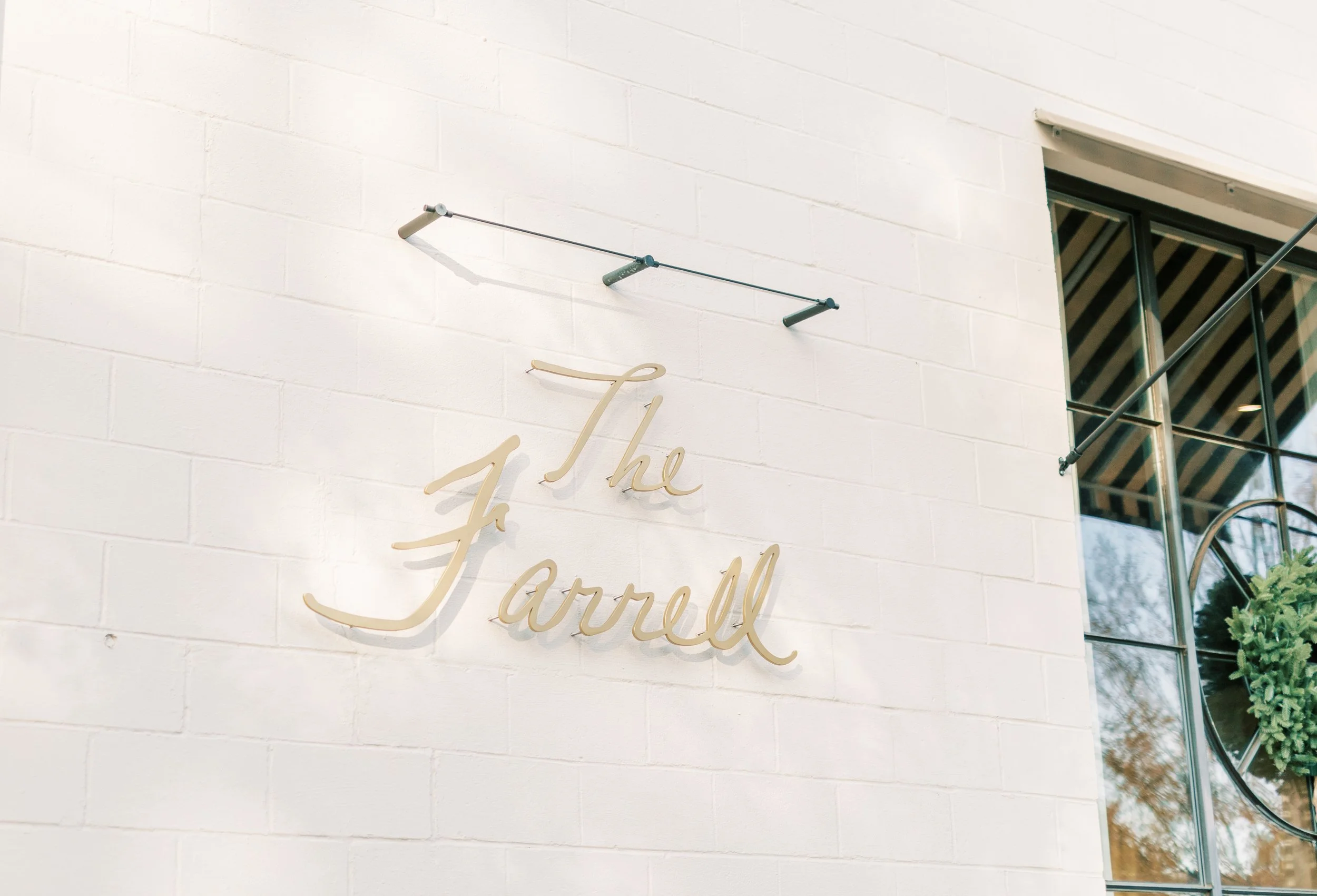A white brick wall with a beige cursive sign that reads "the Jarrell" and a small window with a black frame on the right side.