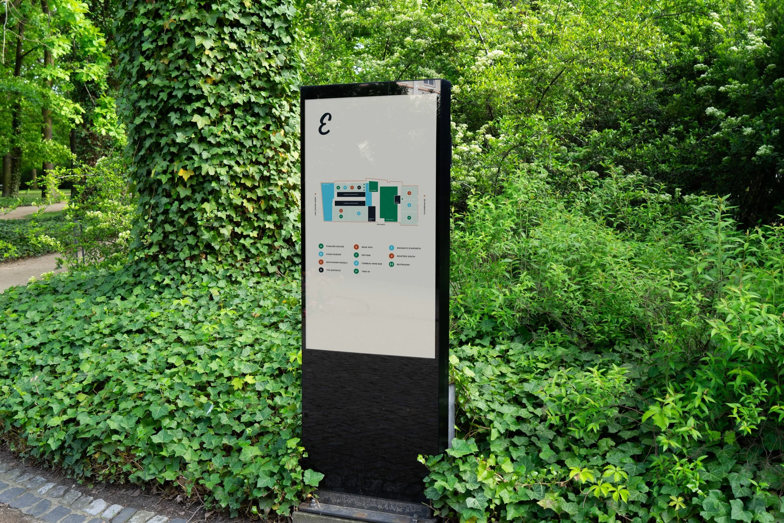 Outdoor park with a large black and white directory sign surrounded by green ivy and trees.