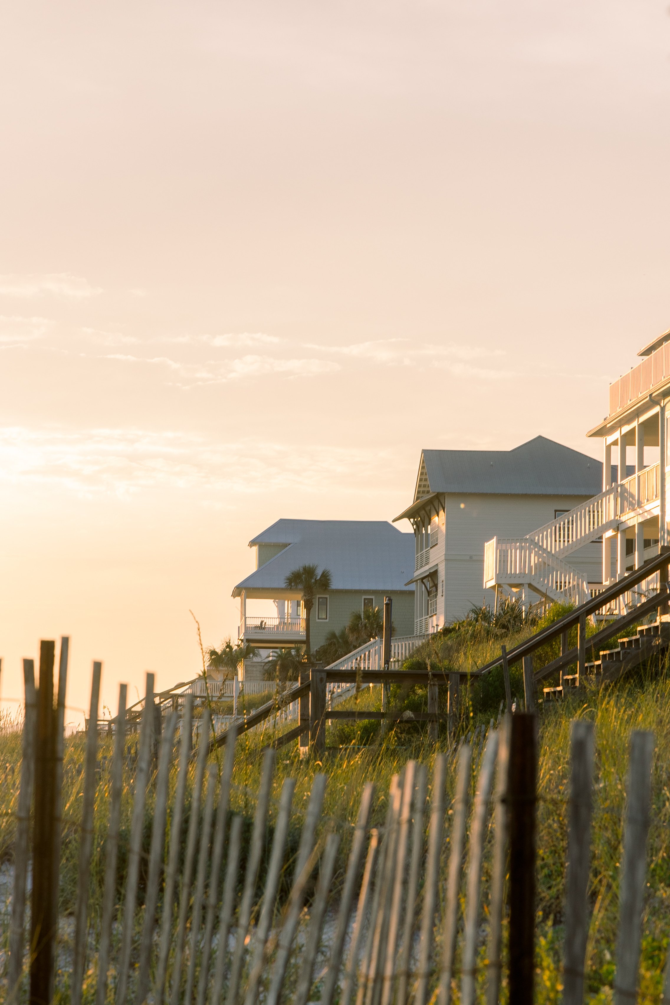 Houses on stilts near the water at sunset, with a pale sky and some clouds.