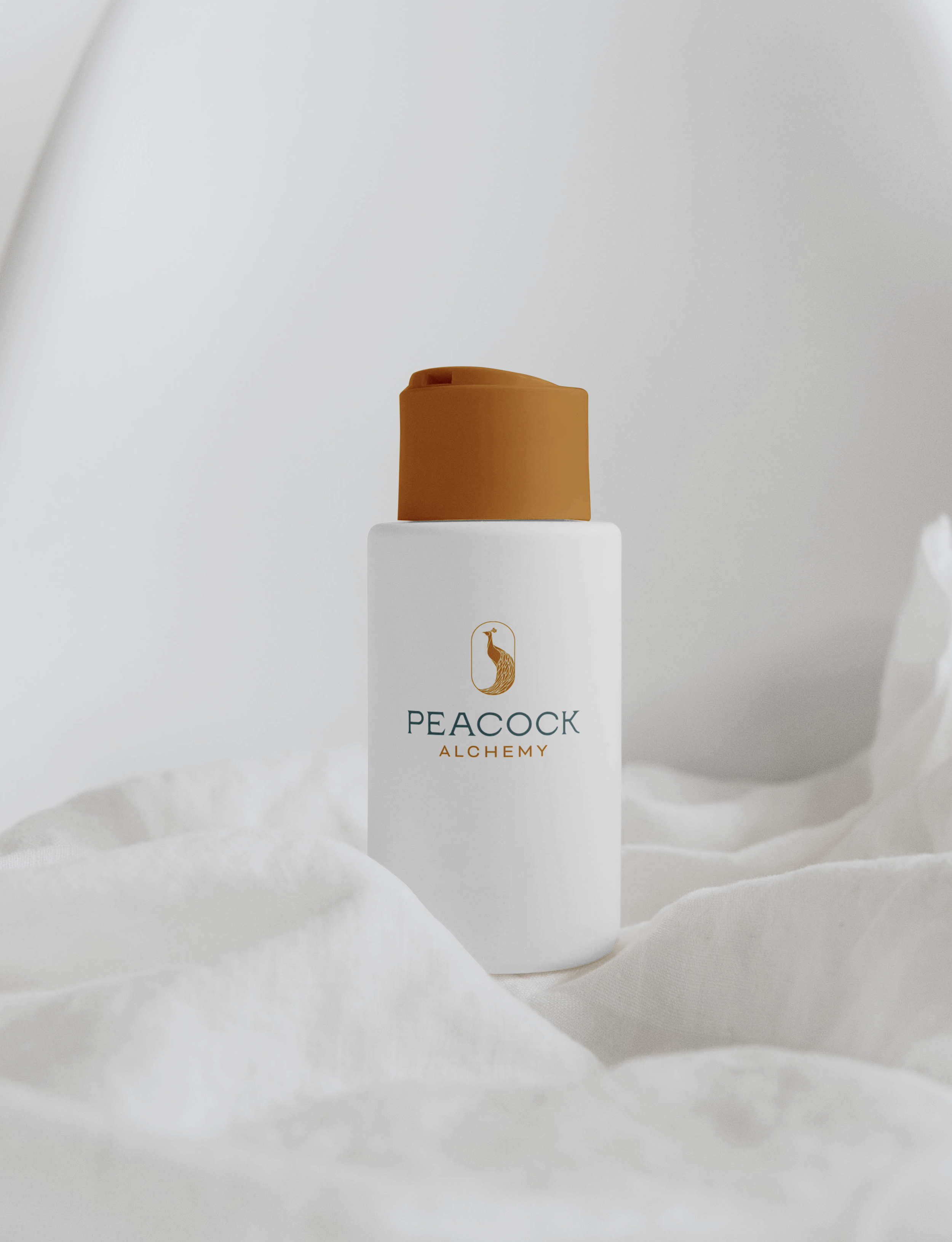 A white box with a gold peacock logo and the word "PEACOCK" printed on it, paired with a tan-colored container with a rounded top, set on a white surface with a white fabric background.