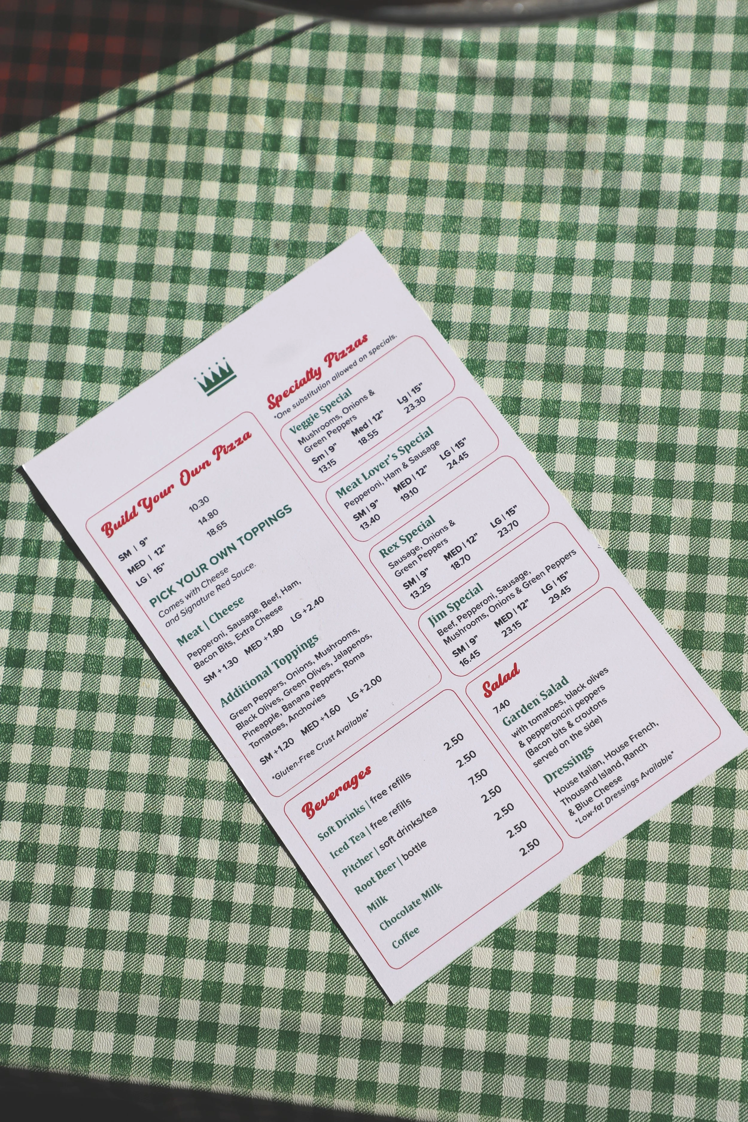 A menu on a white paper with red and green text, placed on a green and white checkered tablecloth.