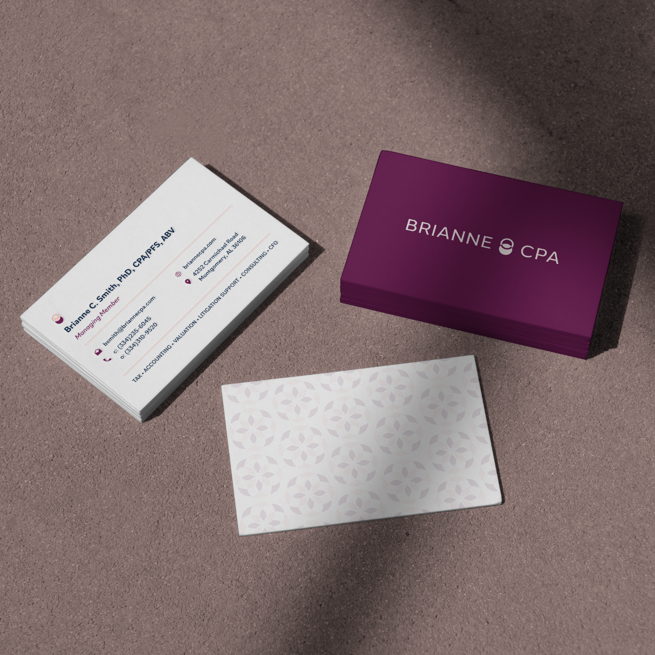 Stack of business cards with one card displaying contact information for Brianna C. Smith, a managing member, and a purple business card holder with the name Brianne CPA. There is also a decorative patterned paper at the bottom of the image, set on a textured surface.