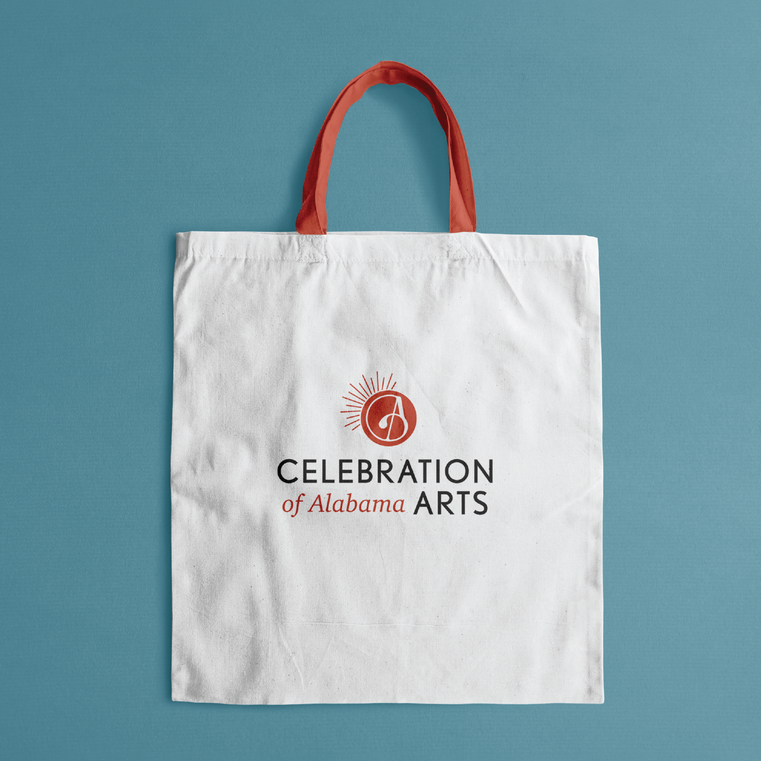 White tote bag with red handles and logo, reading "Celebration of Alabama Arts," on a blue background.