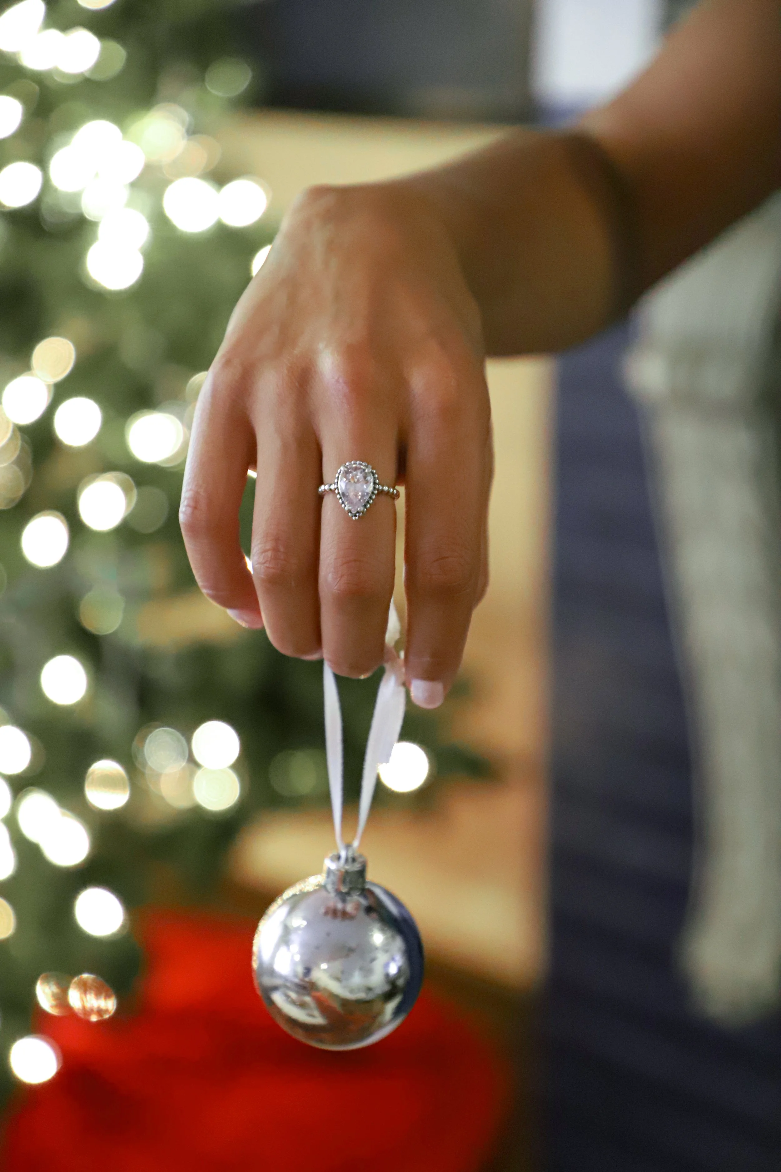 Close-up of a person's hand holding a Christmas ornament in front of a decorated Christmas tree with bokeh lights.