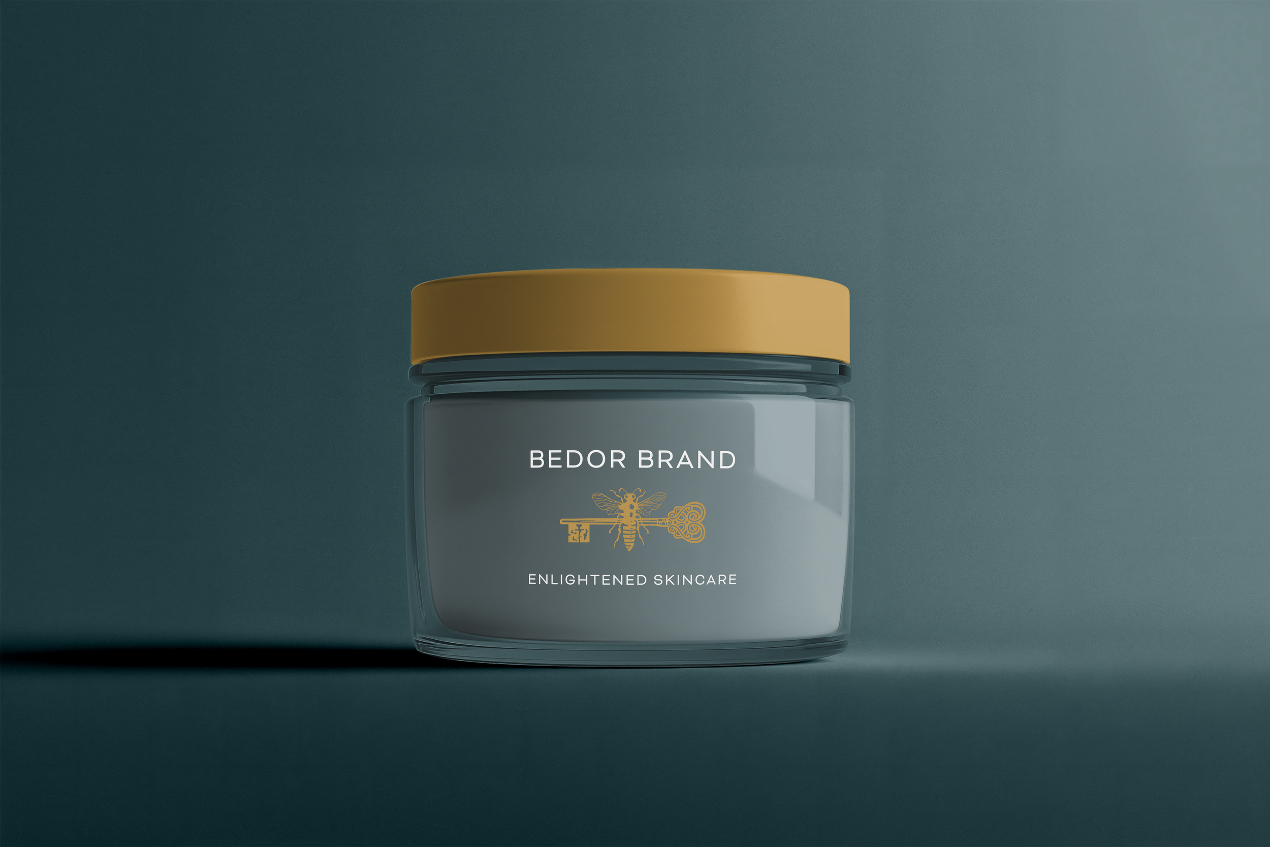 Close-up of a skincare product jar with a yellow lid and a gray body, featuring the text 'BEDOR BRAND' and 'ENLIGHTENED SKINCARE' along with a decorative bee and key logo on a dark background.
