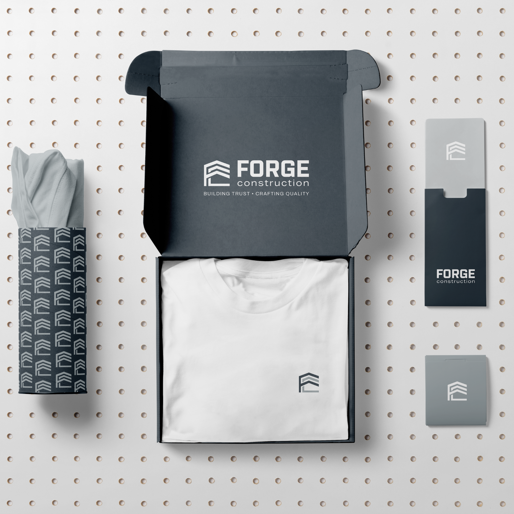 A collection of branded packaging and apparel items from Forge Construction, including a white T-shirt, a tumblers, and boxes, all featuring the company's logo and tagline, arranged on a perforated white background.