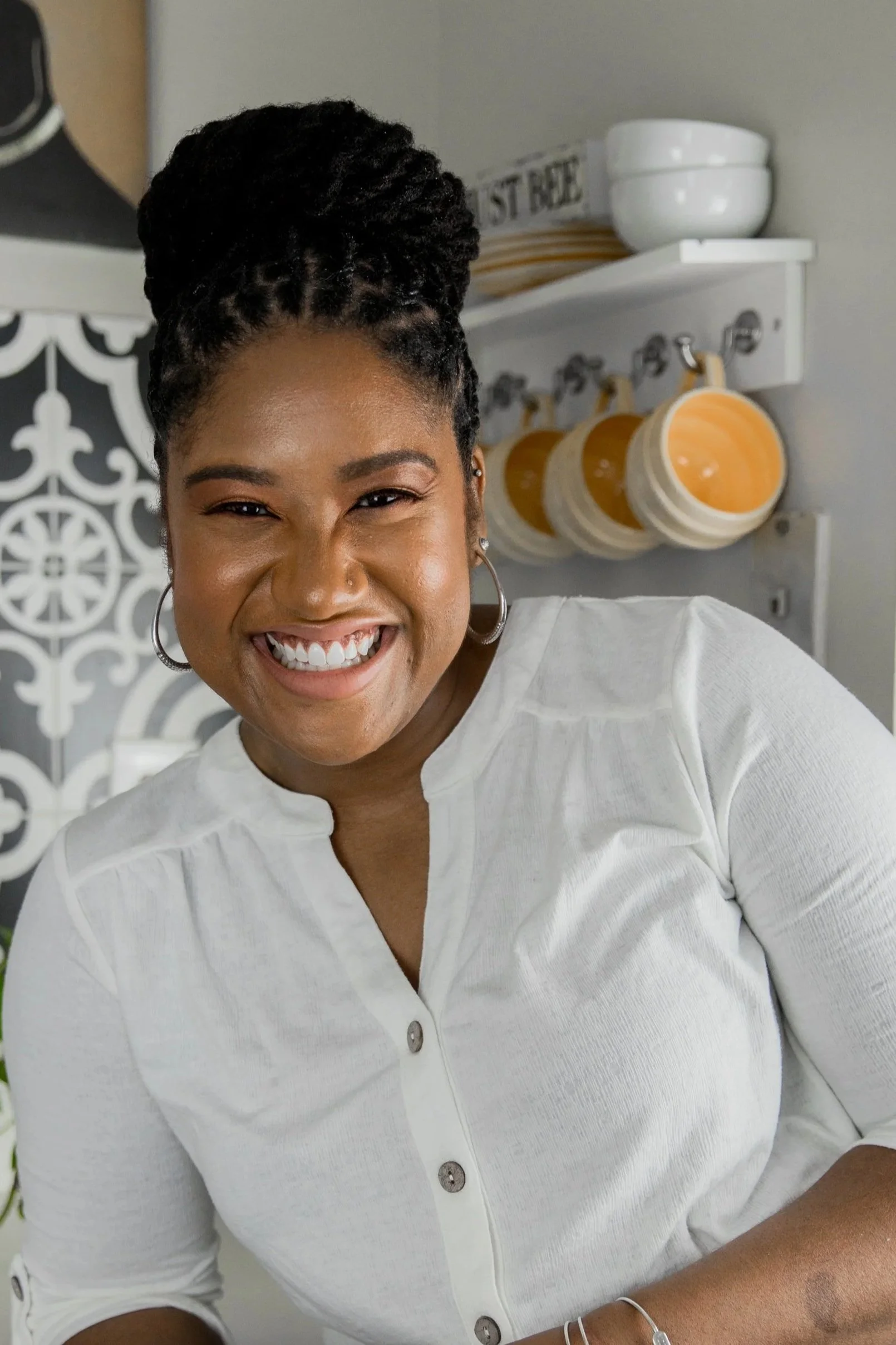 Smiling person with braided updo wearing a blue top and hoop earrings against a plain background.
