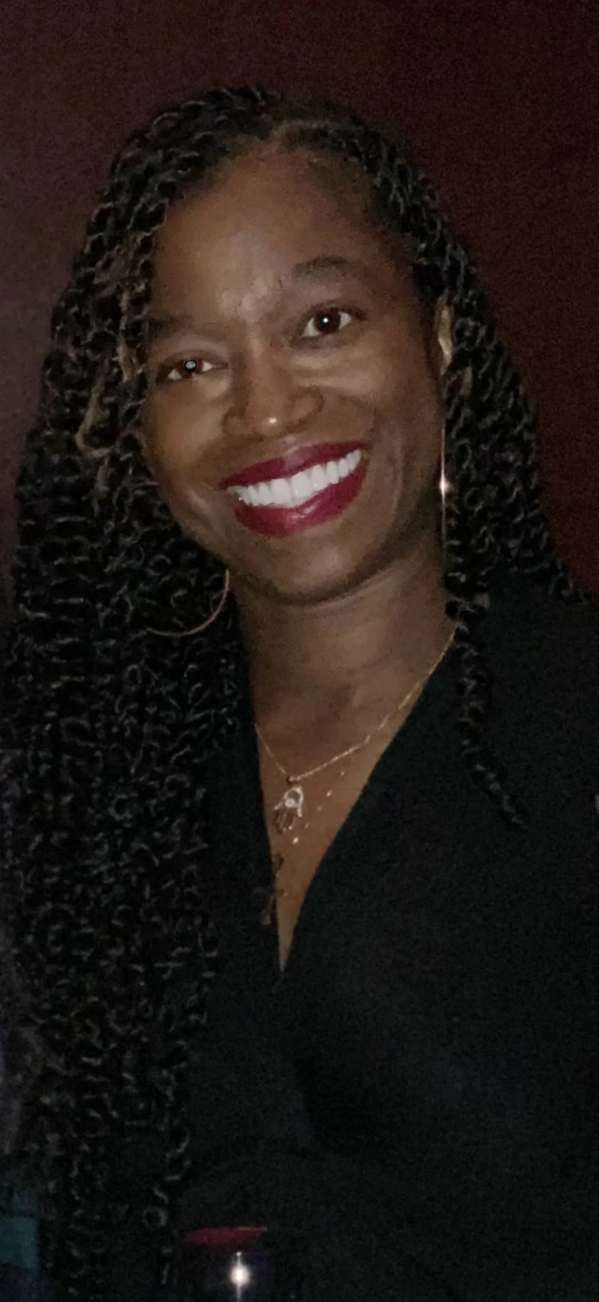 Smiling woman with long hair stands by a railing, wearing a yellow shirt, in front of tropical scenery with palm trees and a vibrant sunset sky.