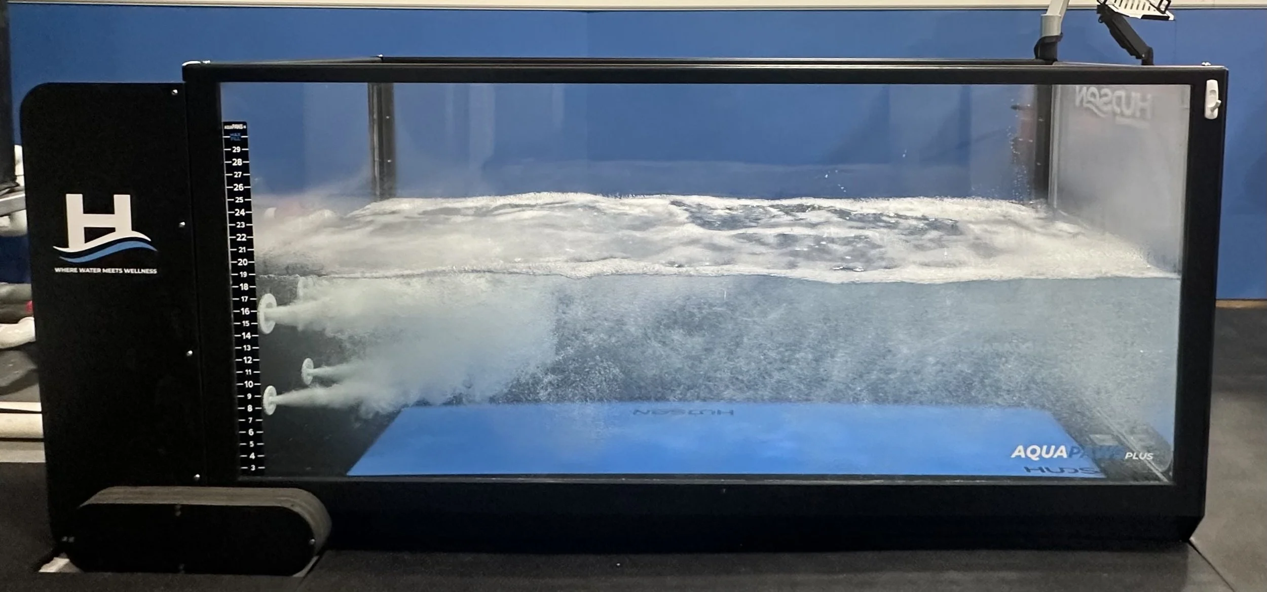 An aqua training tank filled with water and jets creating bubbles and waves, labeled 'AQUA' with a wellness branding logo.