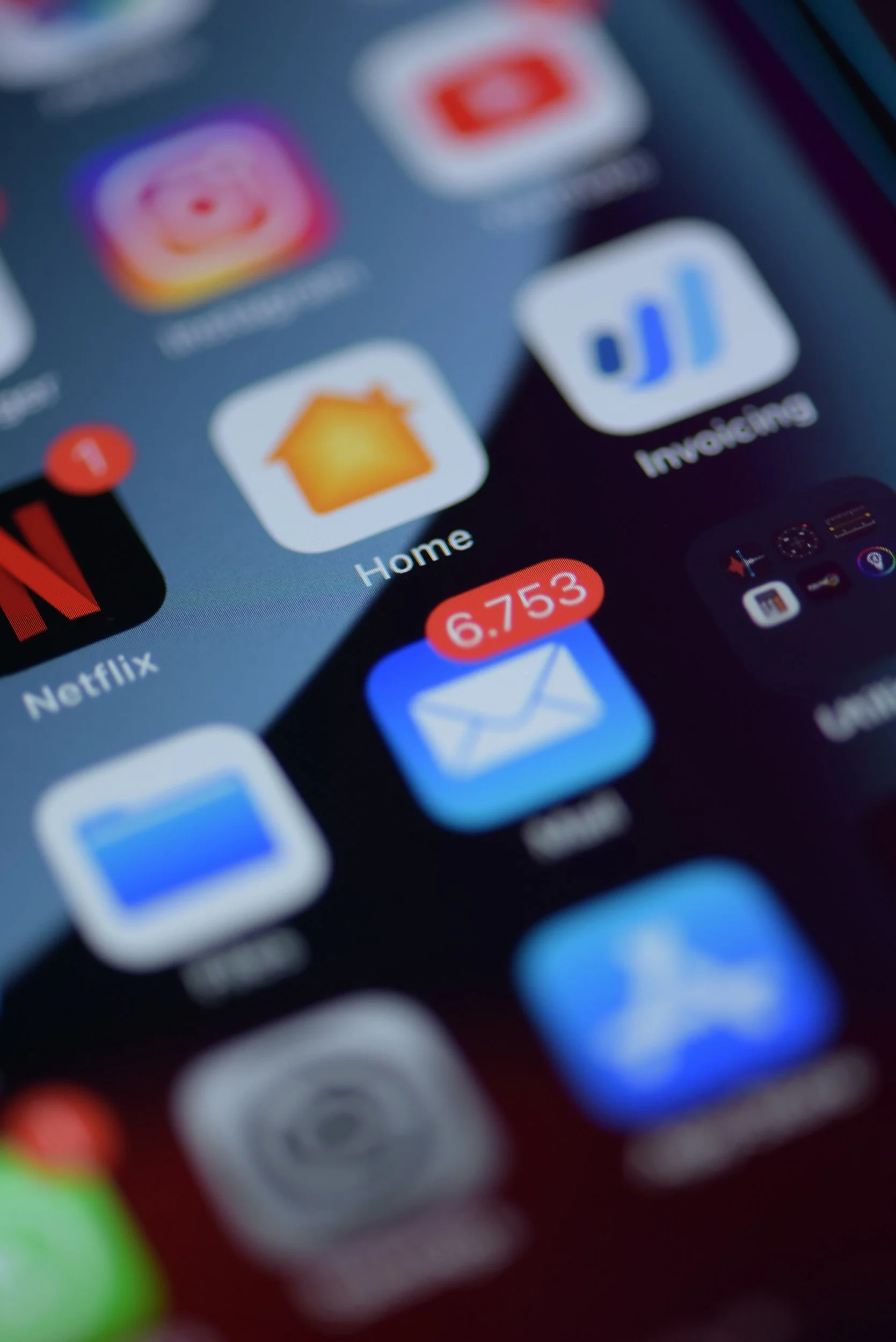 Close-up of a smartphone screen showing various app icons, including Mail with 6,753 unread messages, Netflix, Home, and Invdtunes.