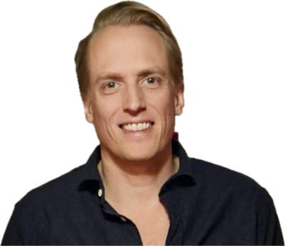 A man with blond hair and a dark shirt smiling against a yellow background.