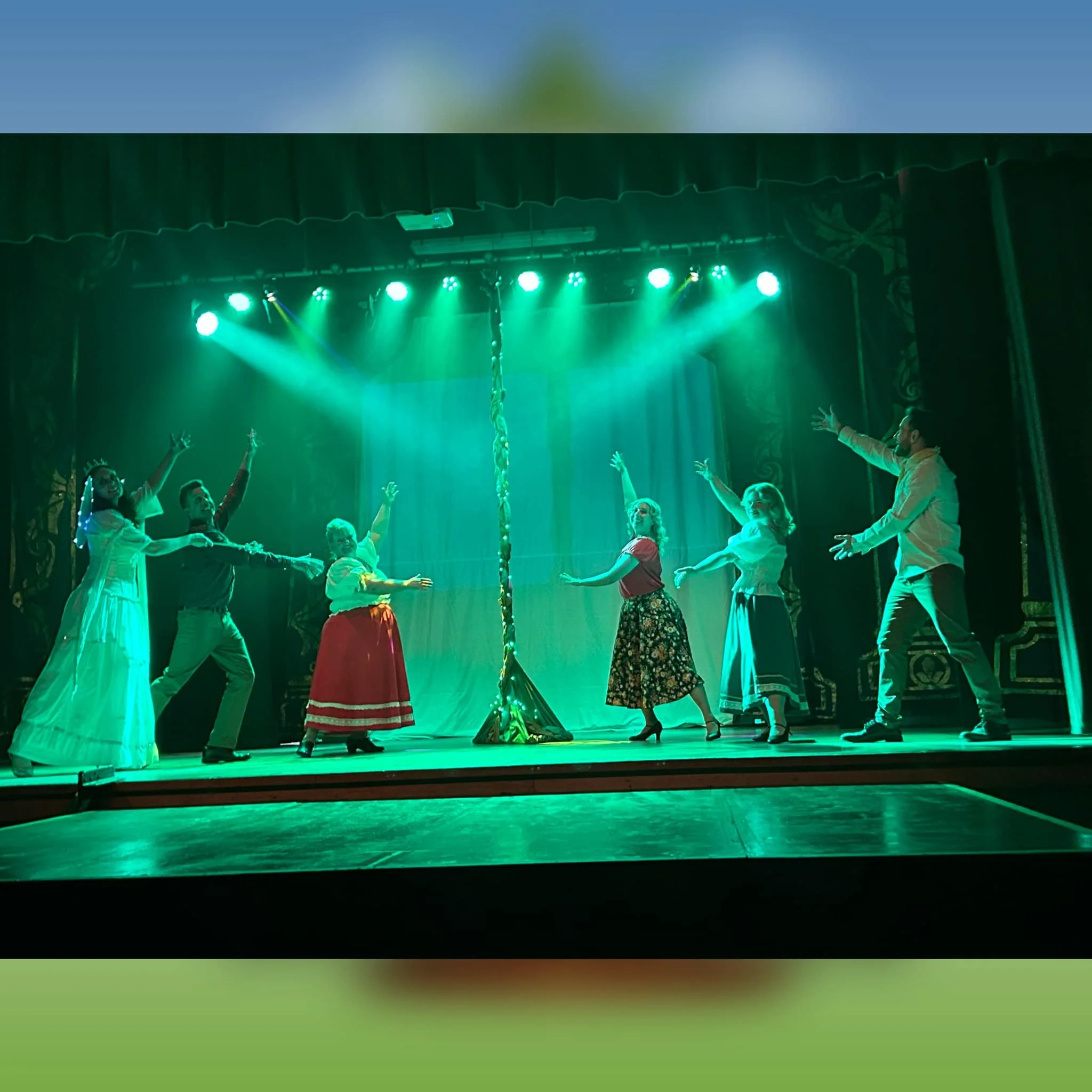 People on stage in old-fashioned costumes performing a dance or play, illuminated by green stage lights, with a curtain backdrop and a decorated pole at center stage.