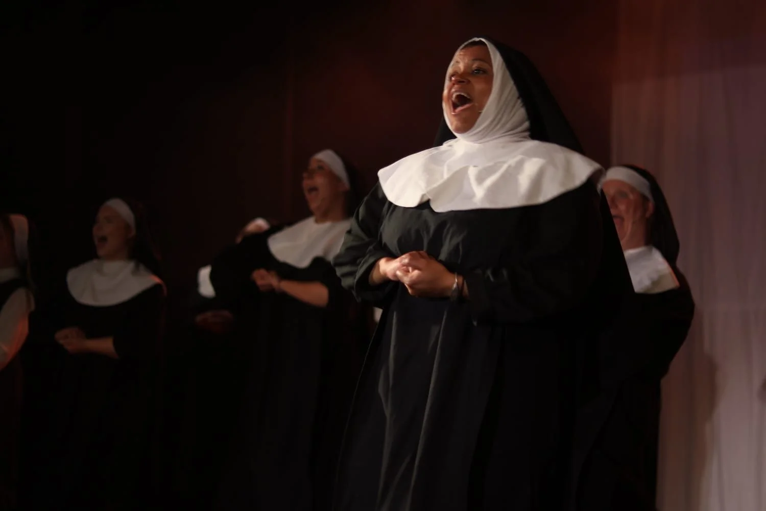 Women dressed as nuns singing or performing together on a stage.
