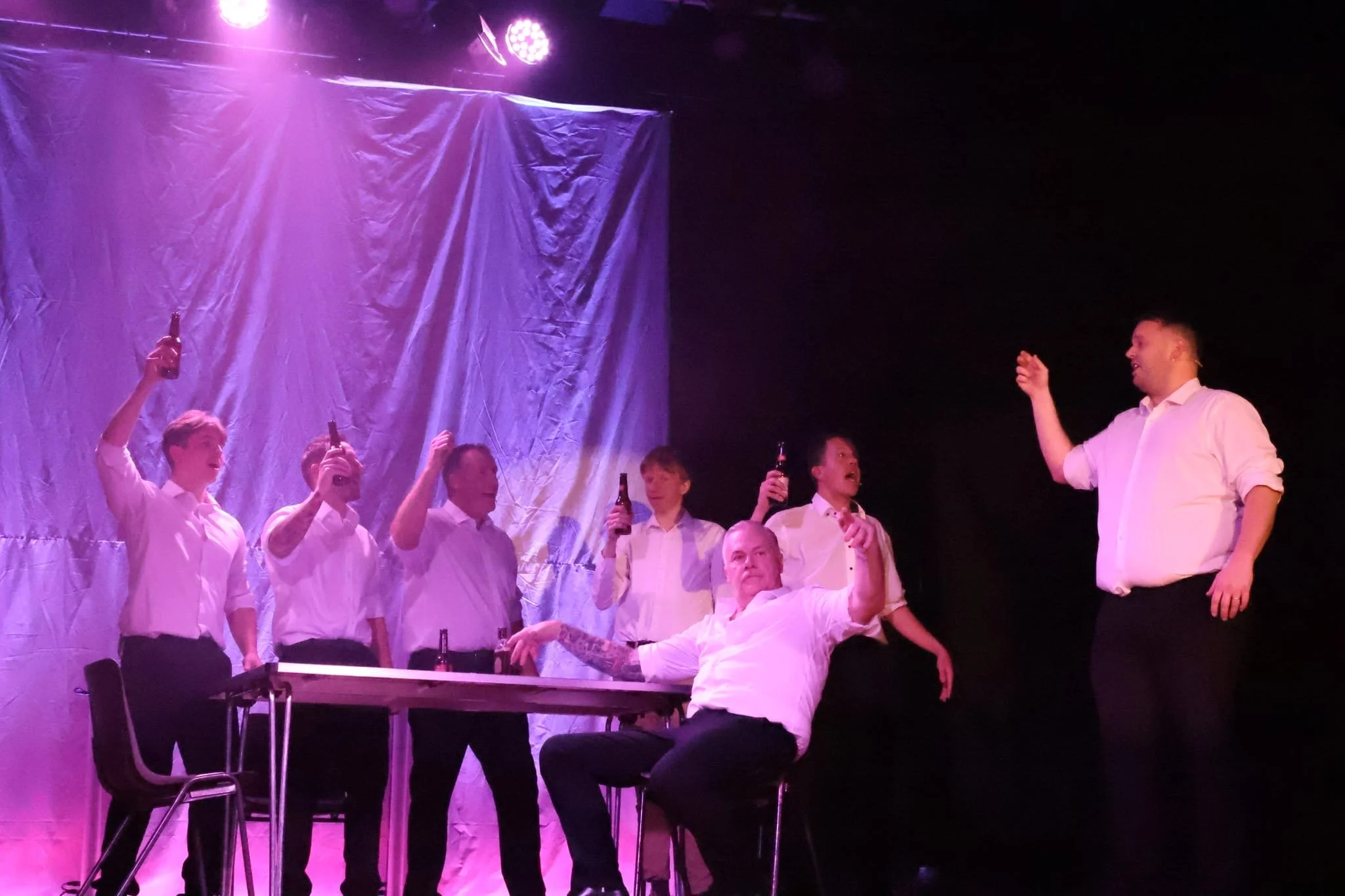 Group of men in white shirts celebrating with drinks in a dark room with purple stage lighting.