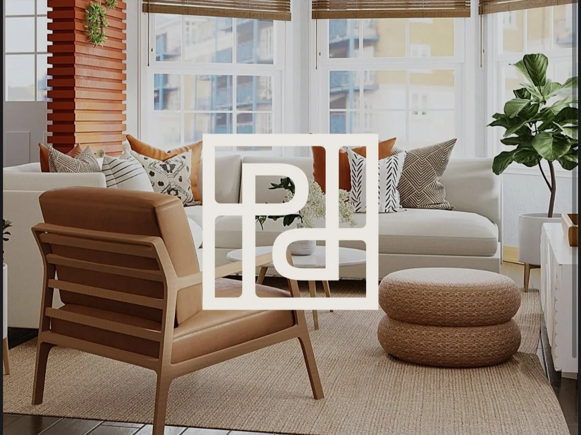 Living room with white sofa decorated with patterned throw pillows, wooden armchair with leather cushion, large potted plant, woven pouf, and large windows with blinds.