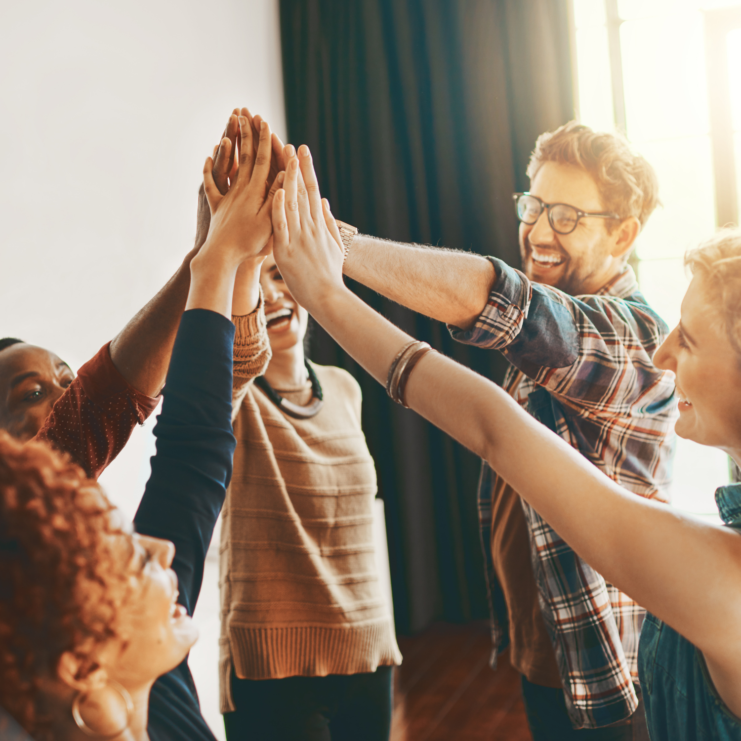 Group of diverse people giving high-five in a cheerful indoor setting.