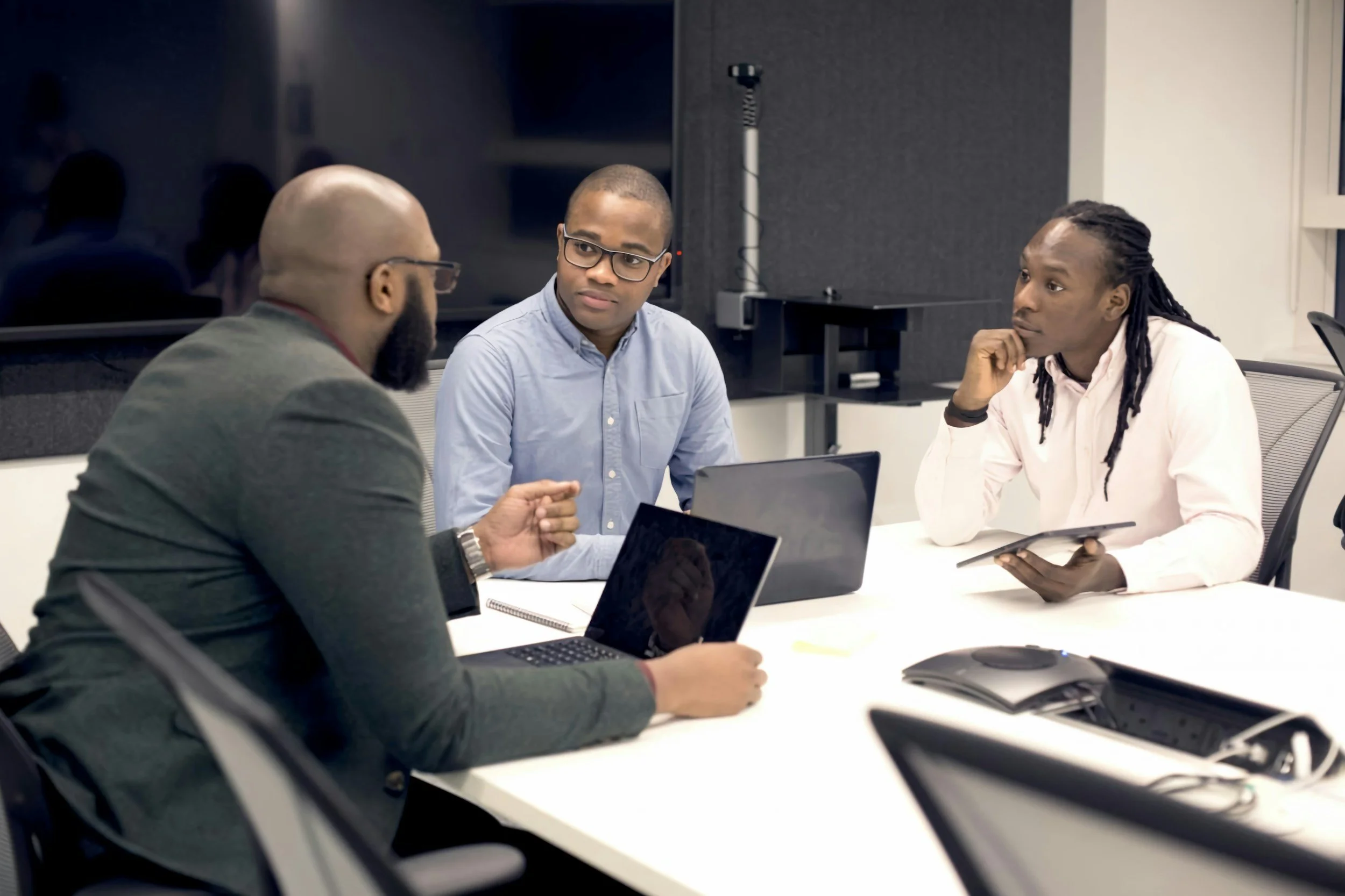 Three men having a business meeting in a conference room with laptops and tablets.