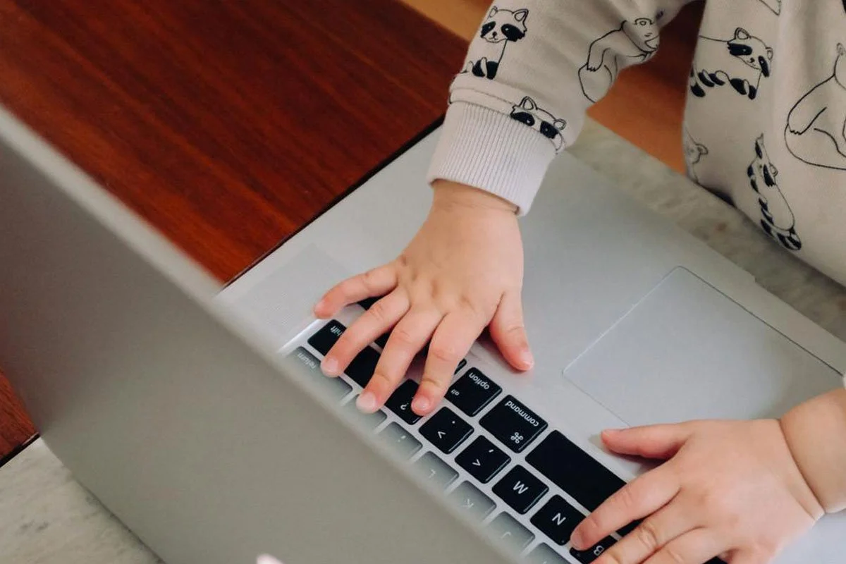 Kleine Kinderhände spielen mit der Tastatur eines Laptops.