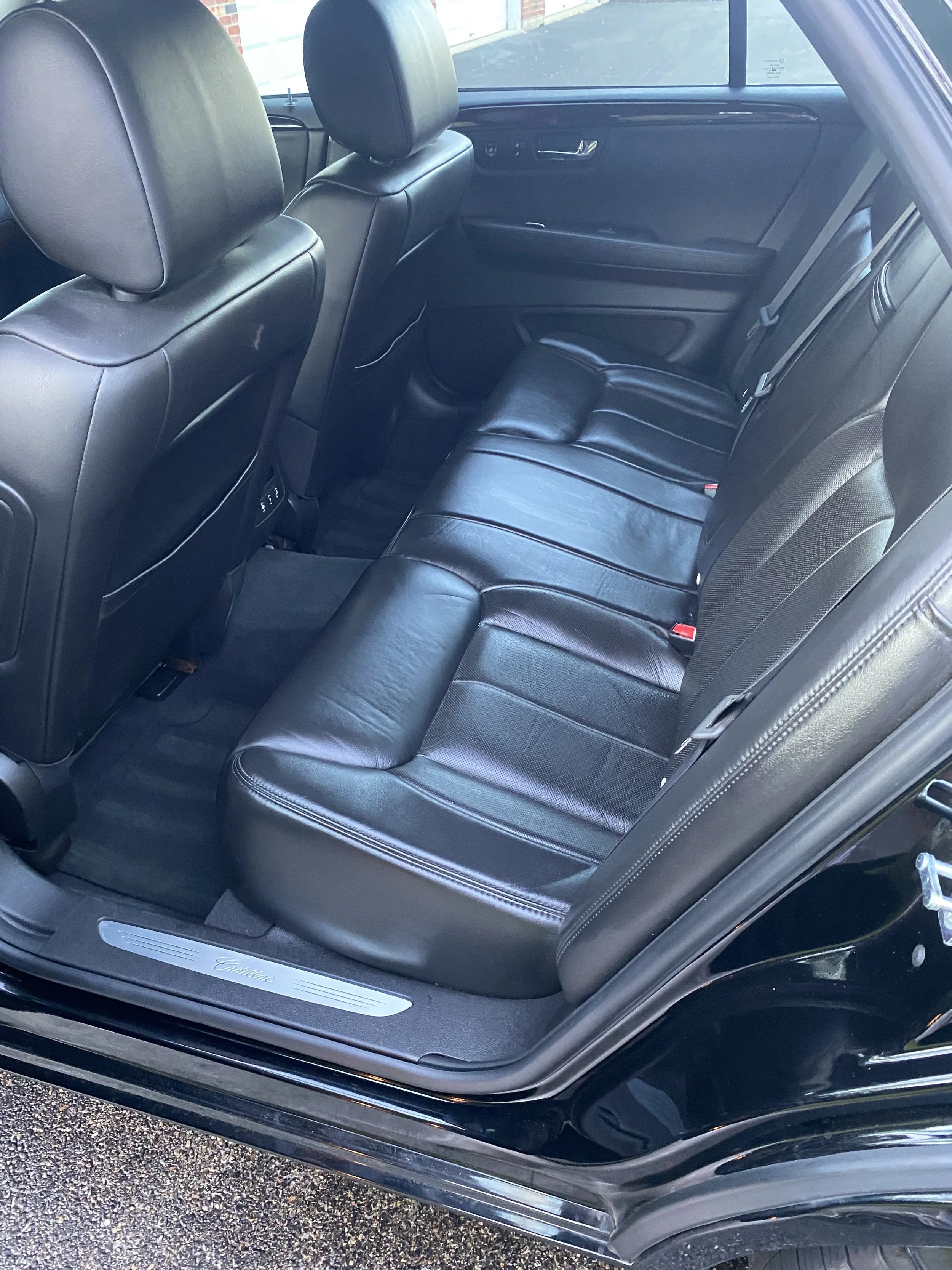 The back seat area of a black leather car interior with three seats, headrests, and a door panel on the right side.