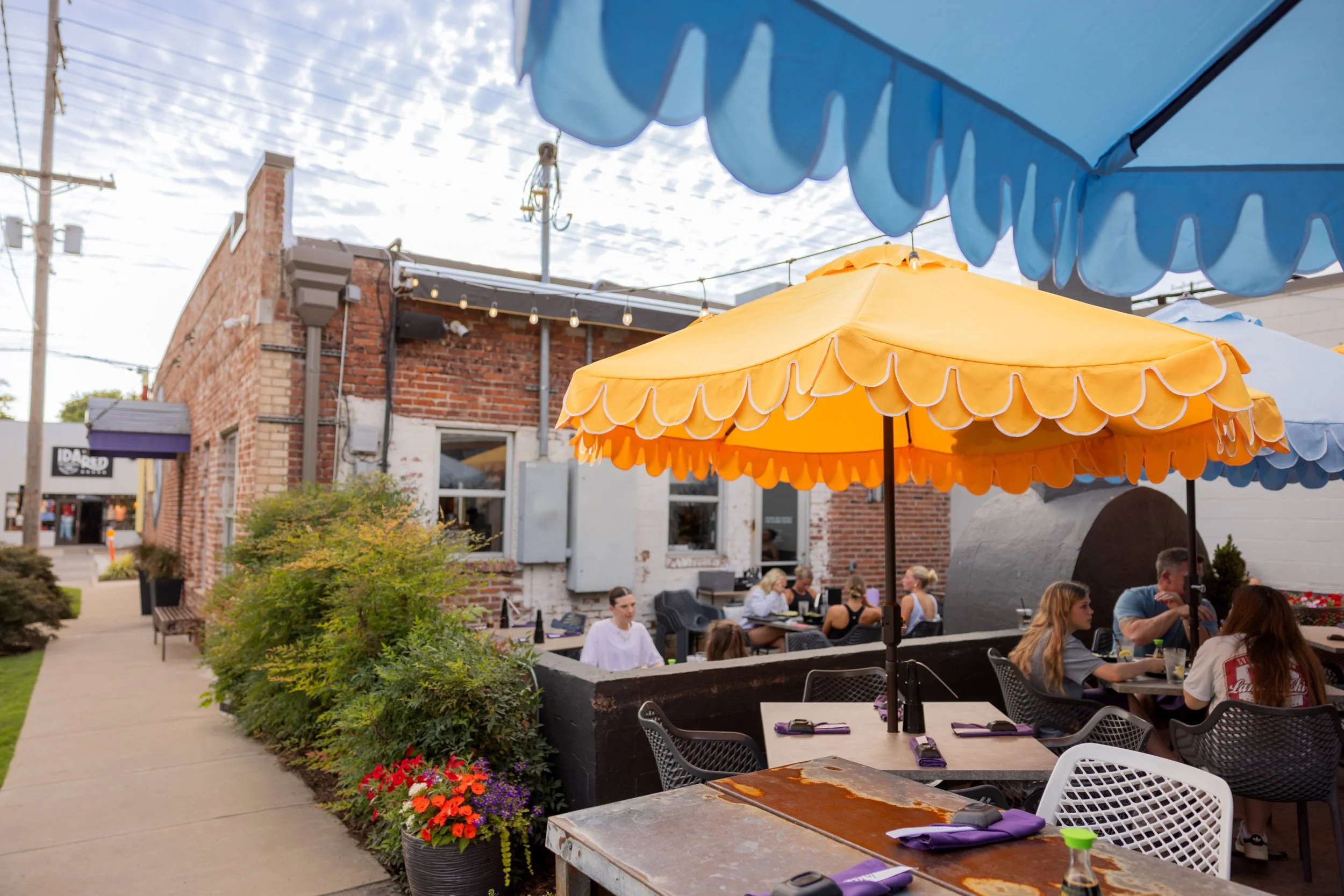 People dining outdoors at a restaurant with colorful umbrellas on a sidewalk in the daytime.