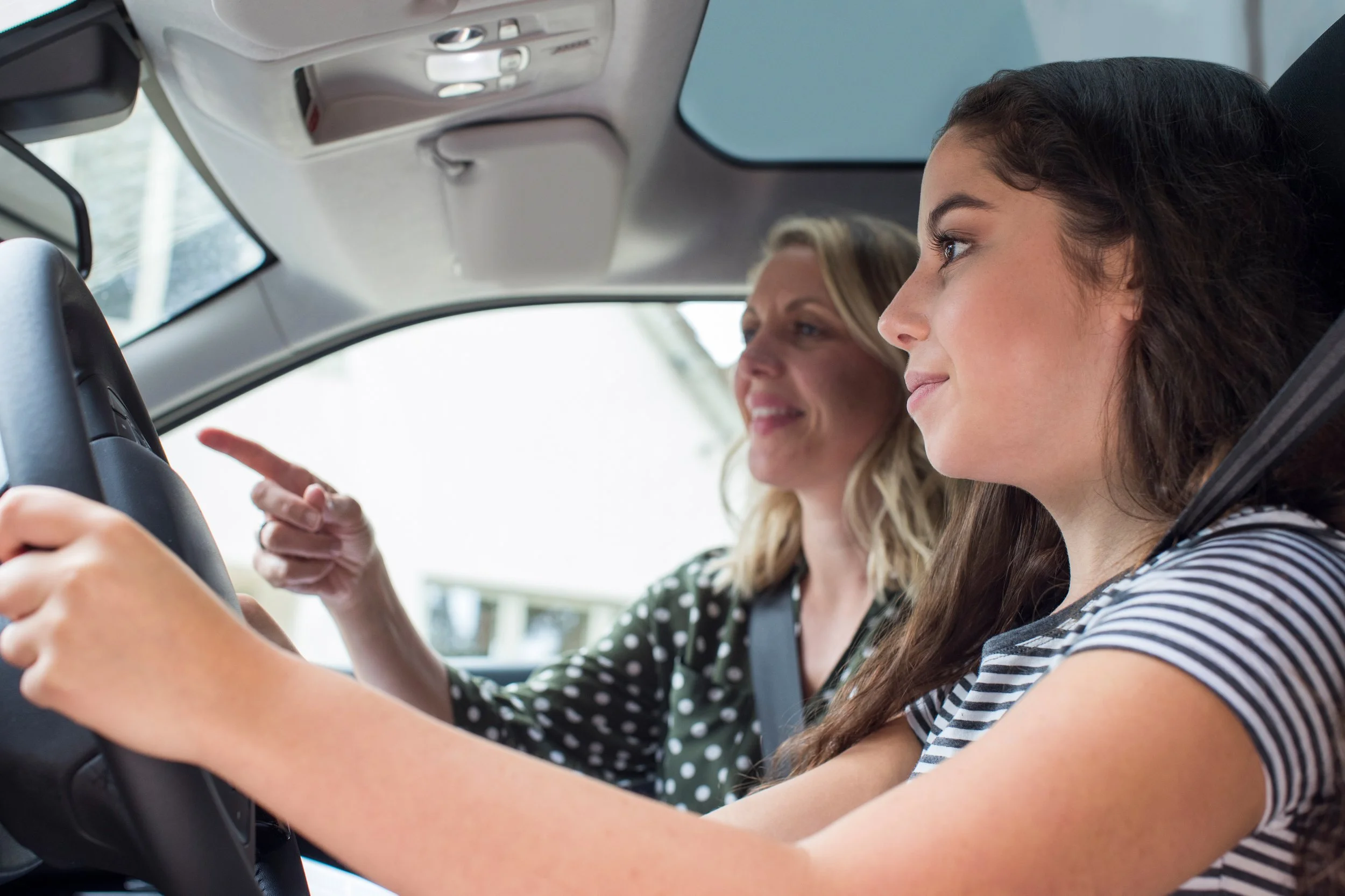 Instructor teaching female student how to drive, female student leaning to drive