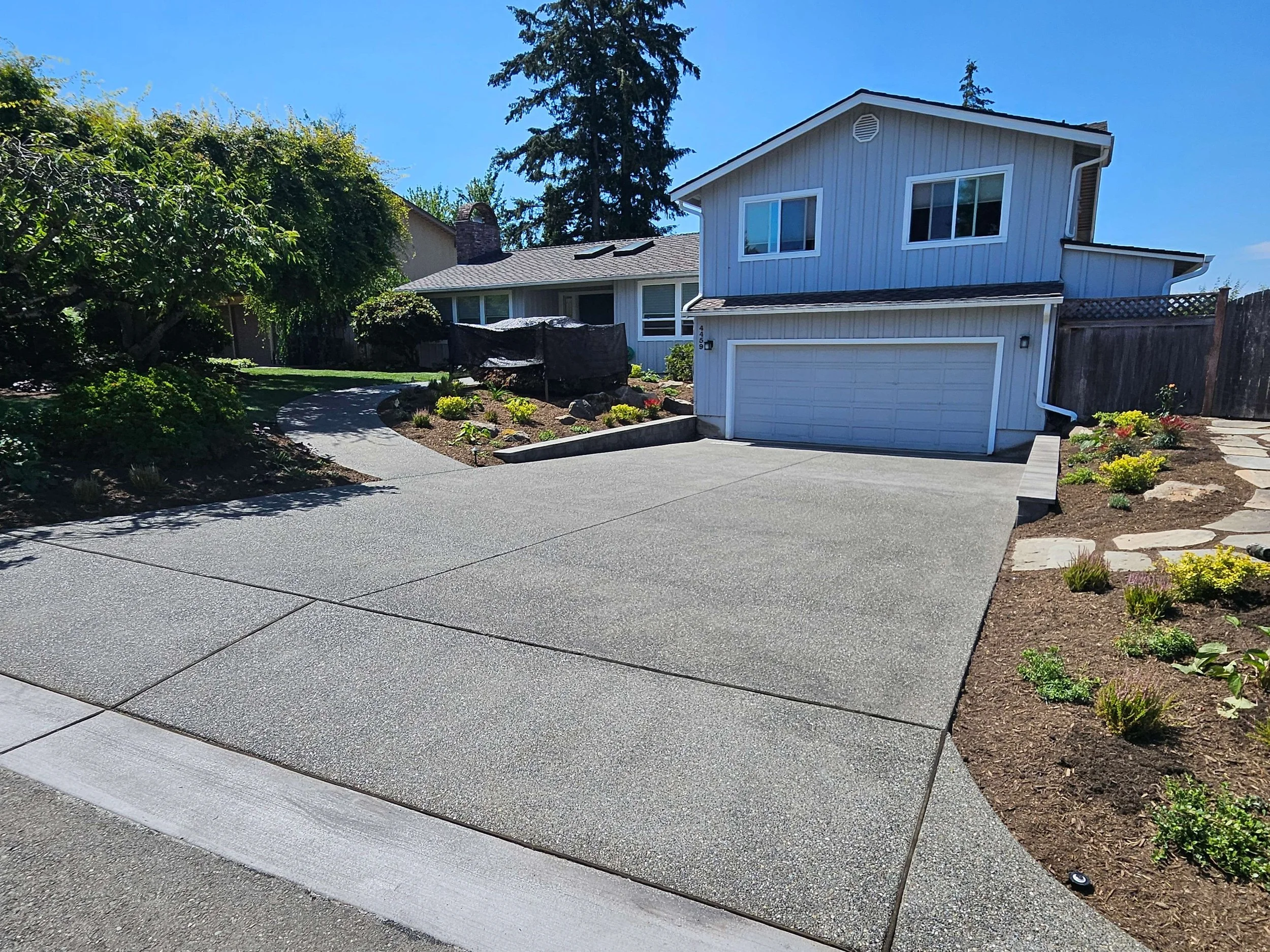 A residential house with a new driveway and landscaped front yard in a suburban neighborhood under a clear blue sky.