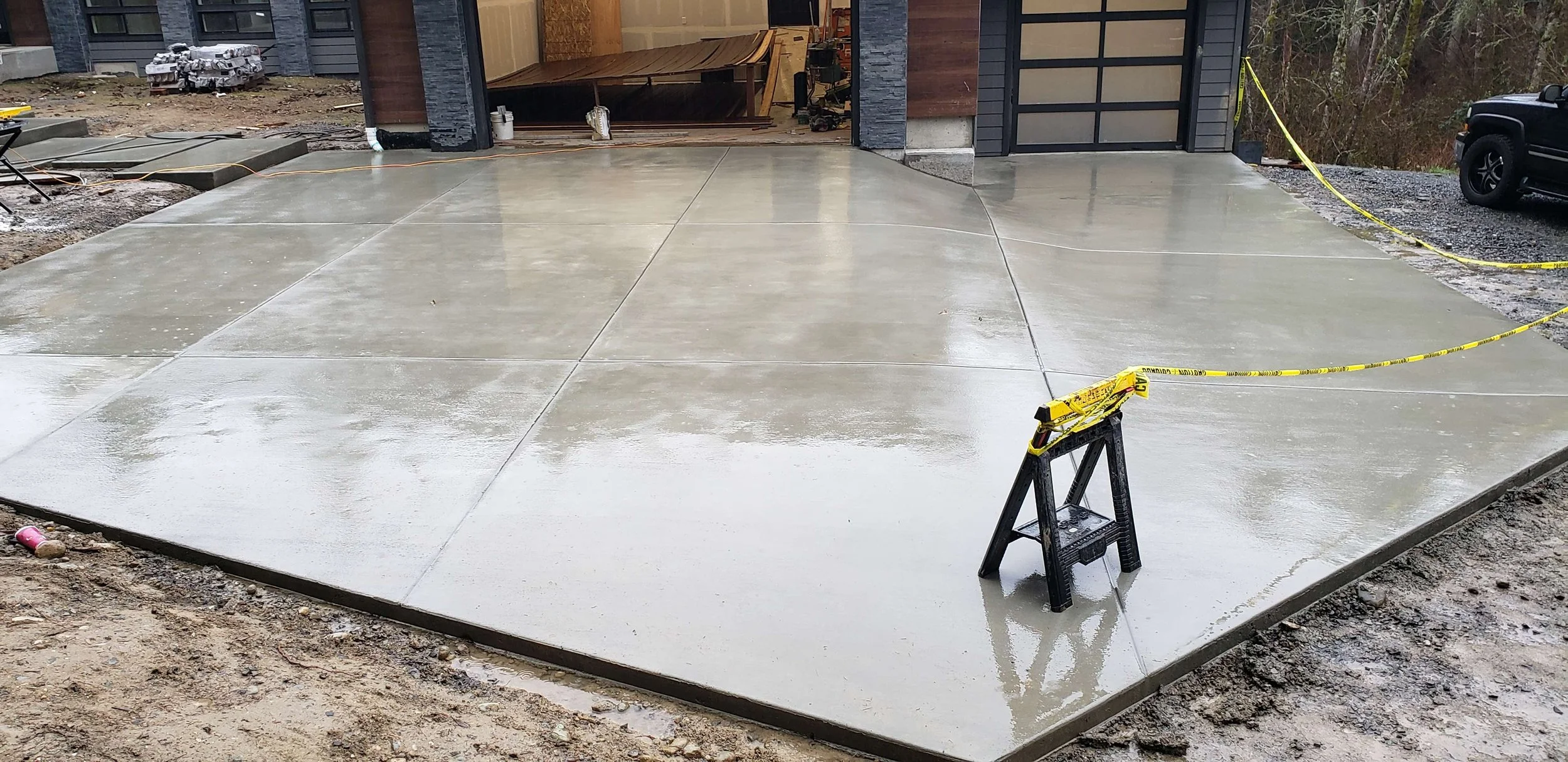 Wet concrete driveway with construction barrier and caution tape in front of a garage for new construction or renovation.