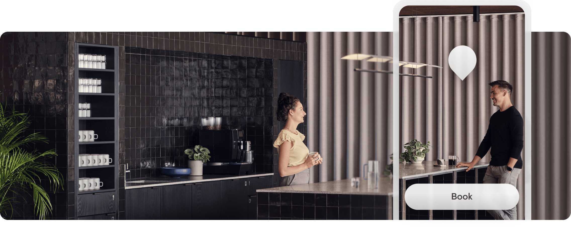 A woman and a man are having a conversation in a modern kitchen with black tiled walls, white cups on black shelves, and beige curtains. The woman, holding a mug, is smiling at the man, who is leaning on a counter with a drink. There is a potted plant on the counter and hanging light fixtures above.