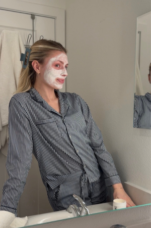 Person with ghost makeup in pajamas looking into a bathroom mirror.