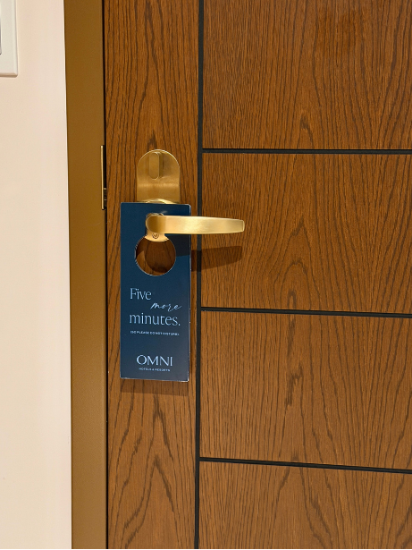 Hotel room door with a brass handle and a blue door hanger that says 'Five more minutes' from OMNI hotel.