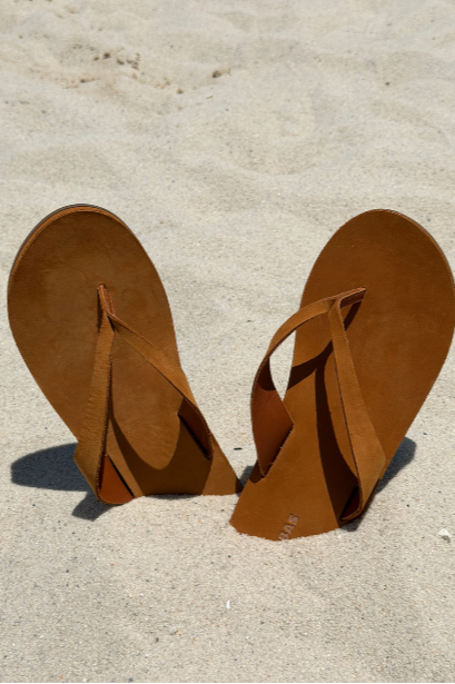 Brown flip-flops standing upright in the sand, creating the appearance of a heart shape.