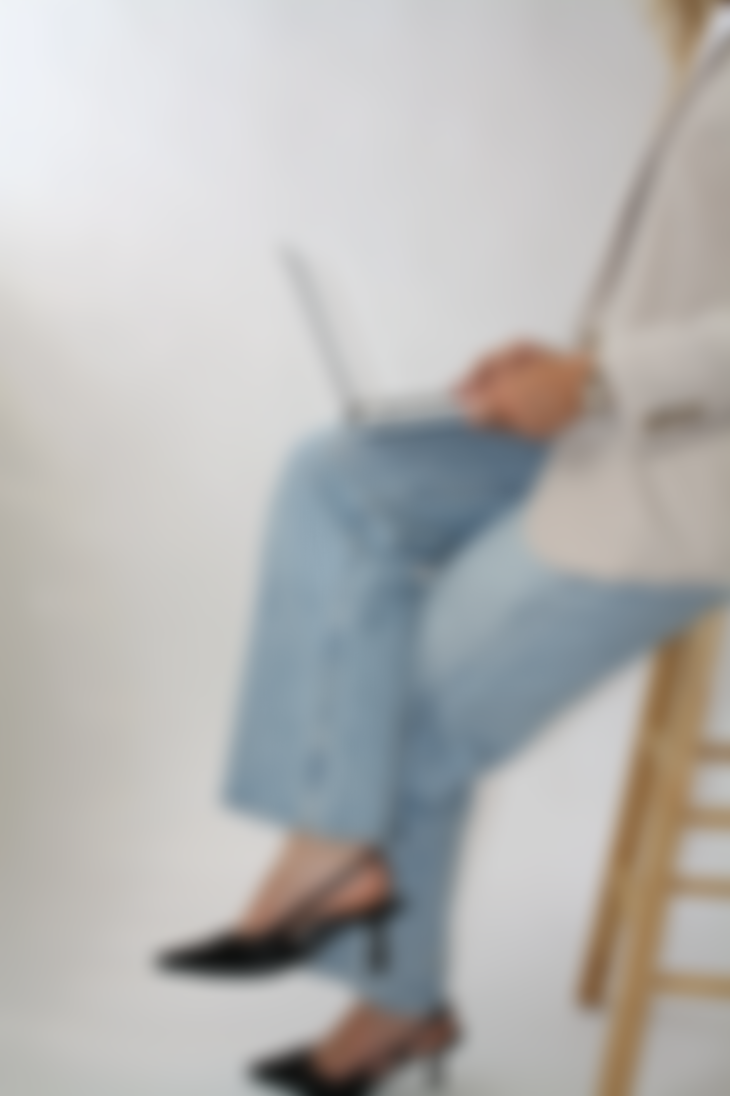 A person standing next to a chair, wearing a white coat, blue jeans, and black shoes, holding a laptop.