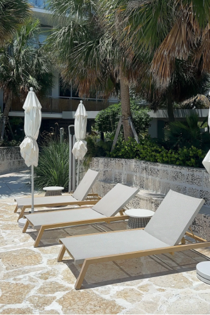 Poolside lounge chairs with umbrellas and tropical plants.