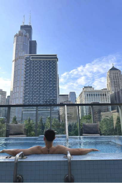 A person relaxing in an outdoor hot tub with Chicago's skyline in the background, including the Willis Tower, on a clear day.