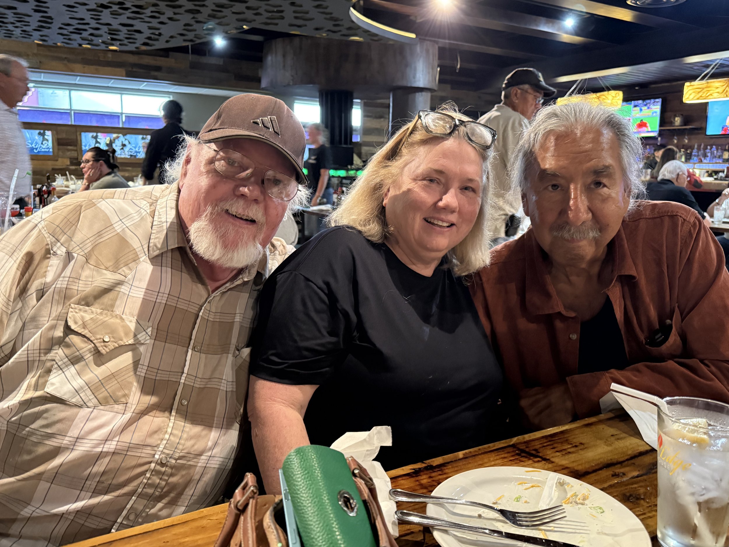 Three smiling people sitting at a restaurant table after a meal, with empty plates and drinks in front of them.