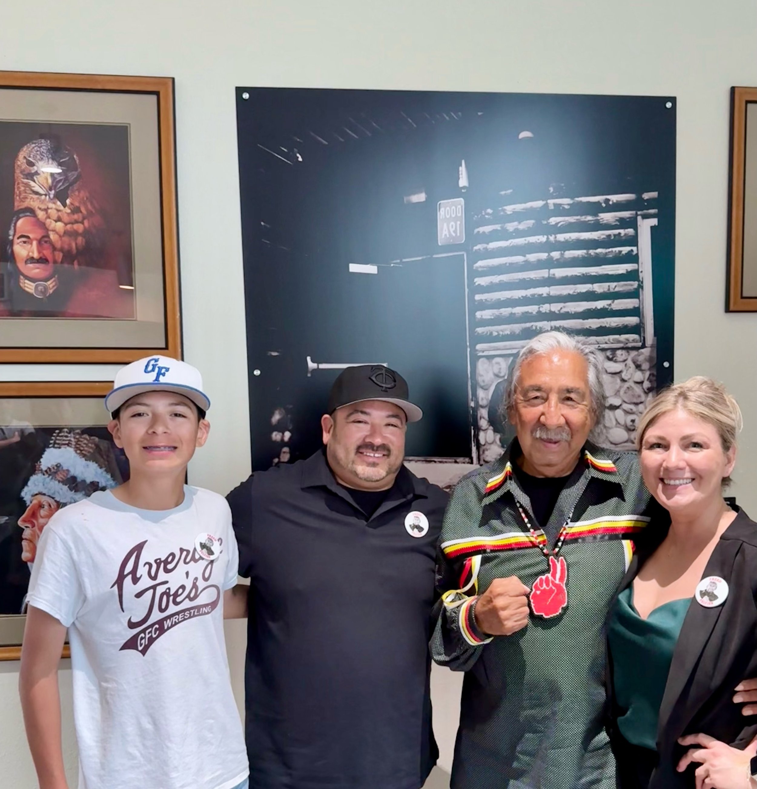 Group of four smiling people posing in front of a black-and-white mural with a mural of a truck and a sign that reads 'ROAD 94.'
