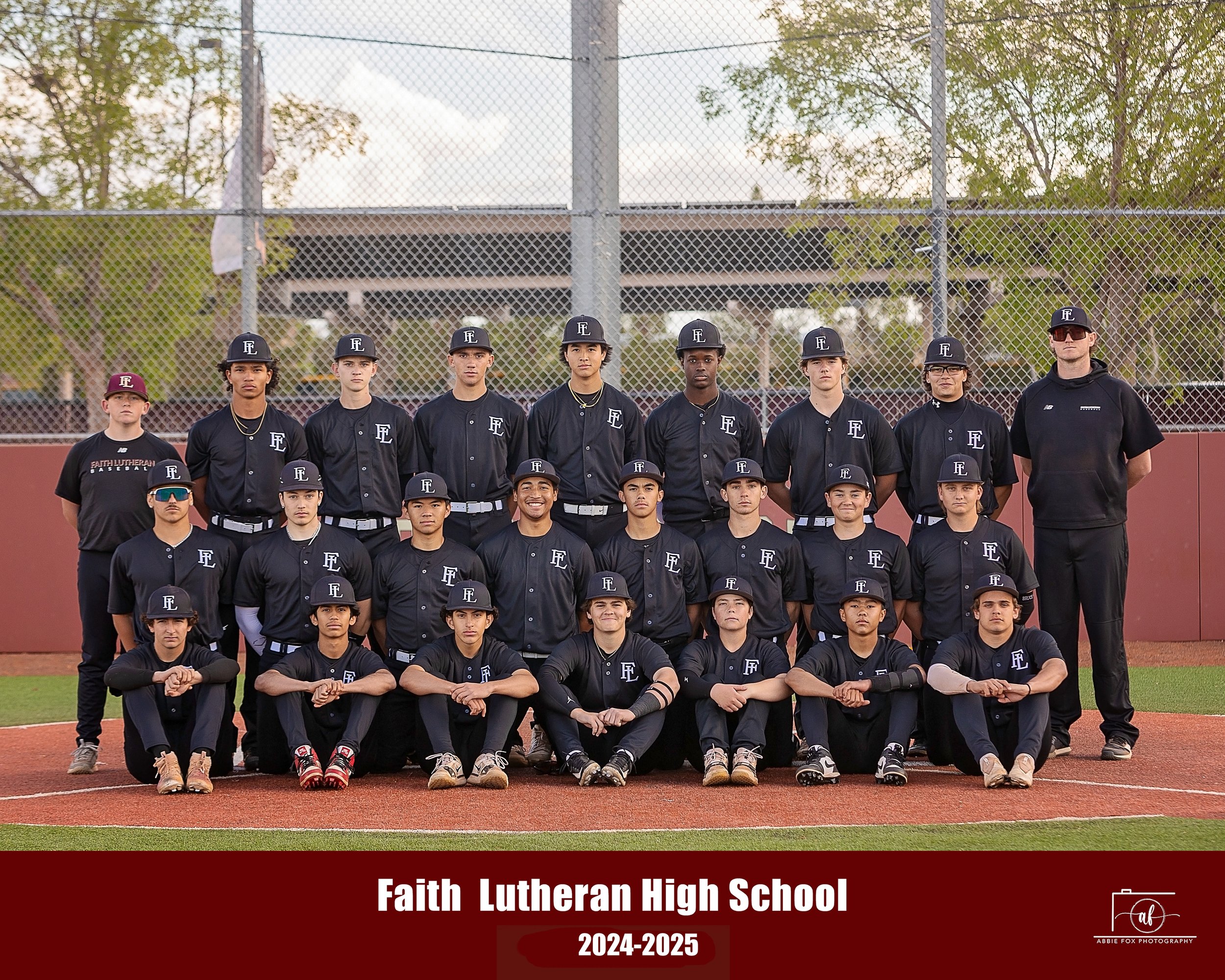 The Faith Lutheran High School baseball team for 2024-2025, with players and coaches, standing on a baseball field behind a chain-link fence during daytime.