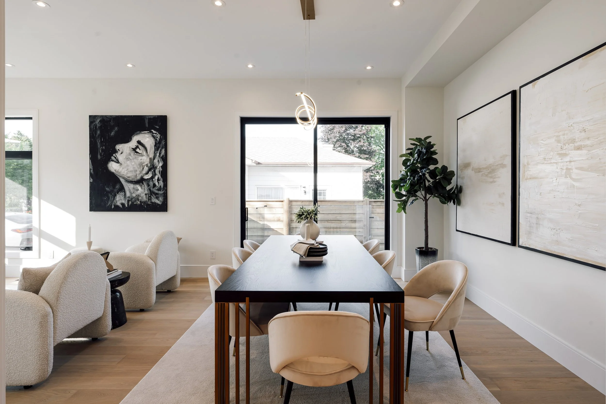 Modern dining room with a black dining table, beige chairs, a large window, and abstract artwork on white walls.