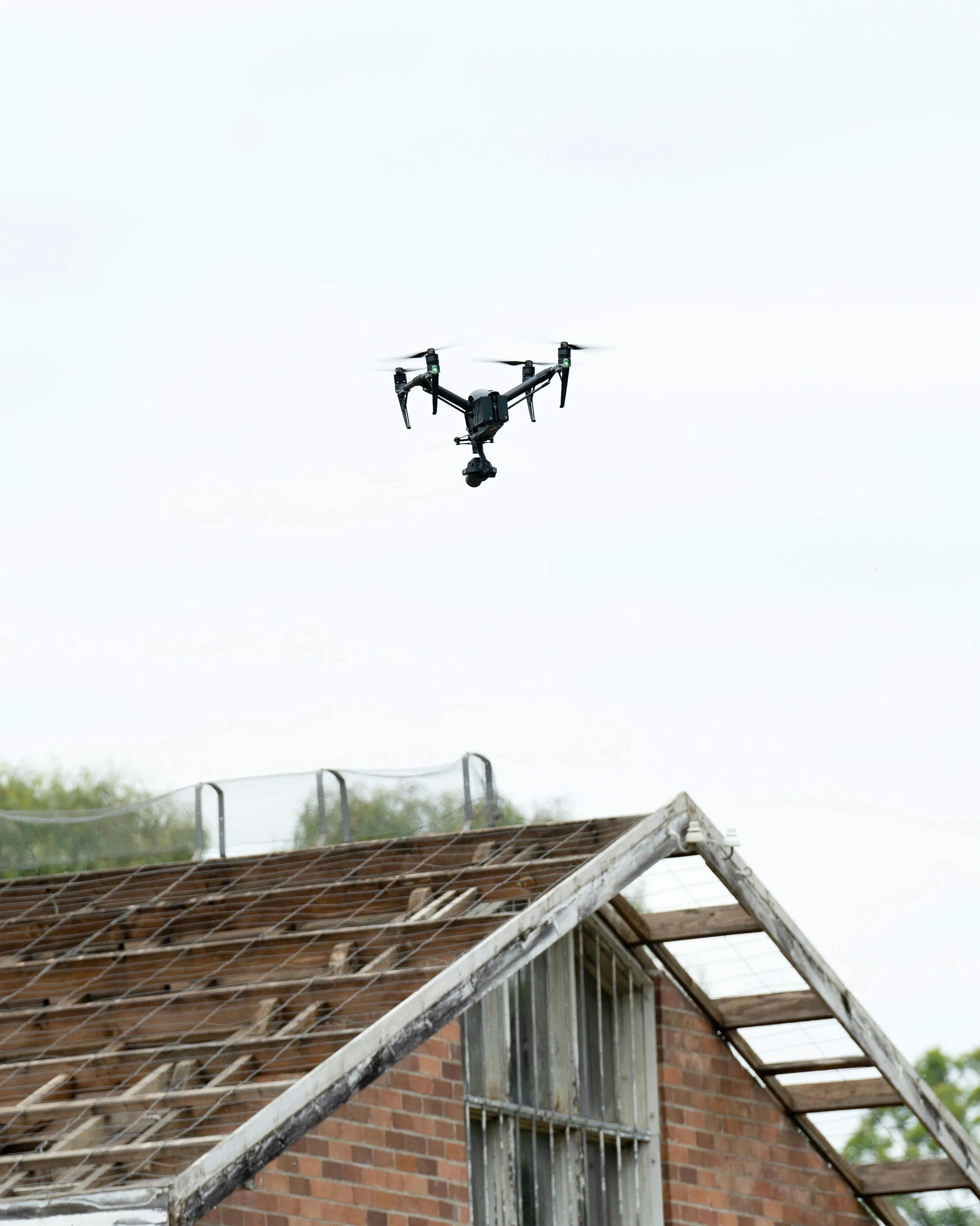 A drone flying above a brick house with a partially broken roof.