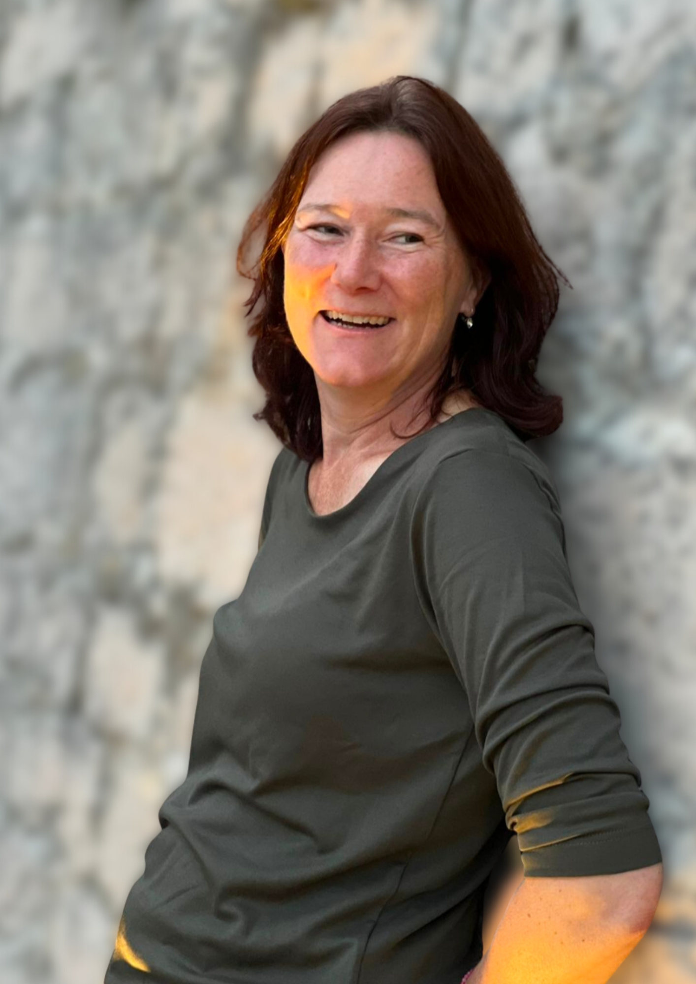 Simone steht lächelnd mit braunen Haaren vor einer Felswand.