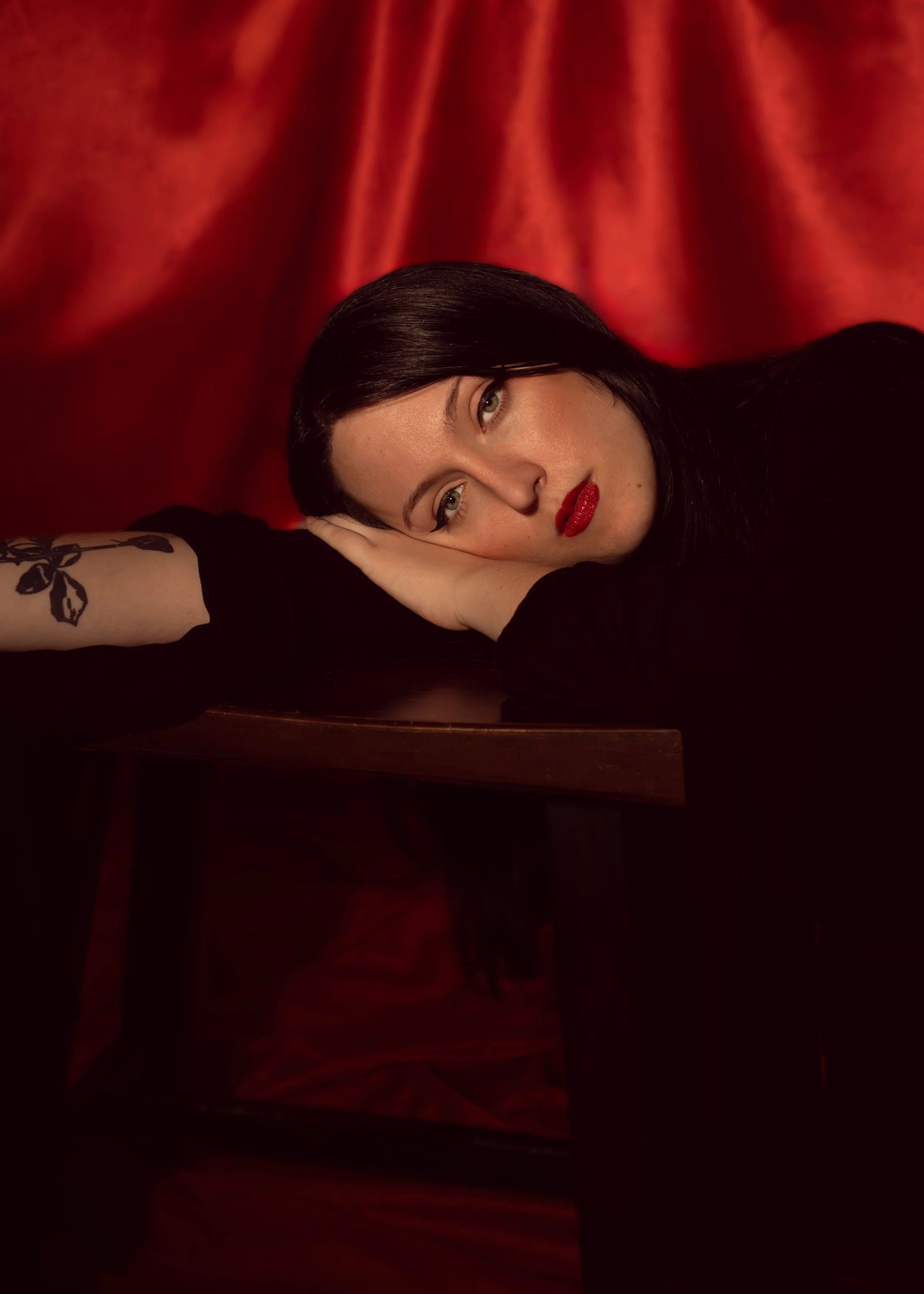 Image of woman laying her head on a small stool against a red backdrop.