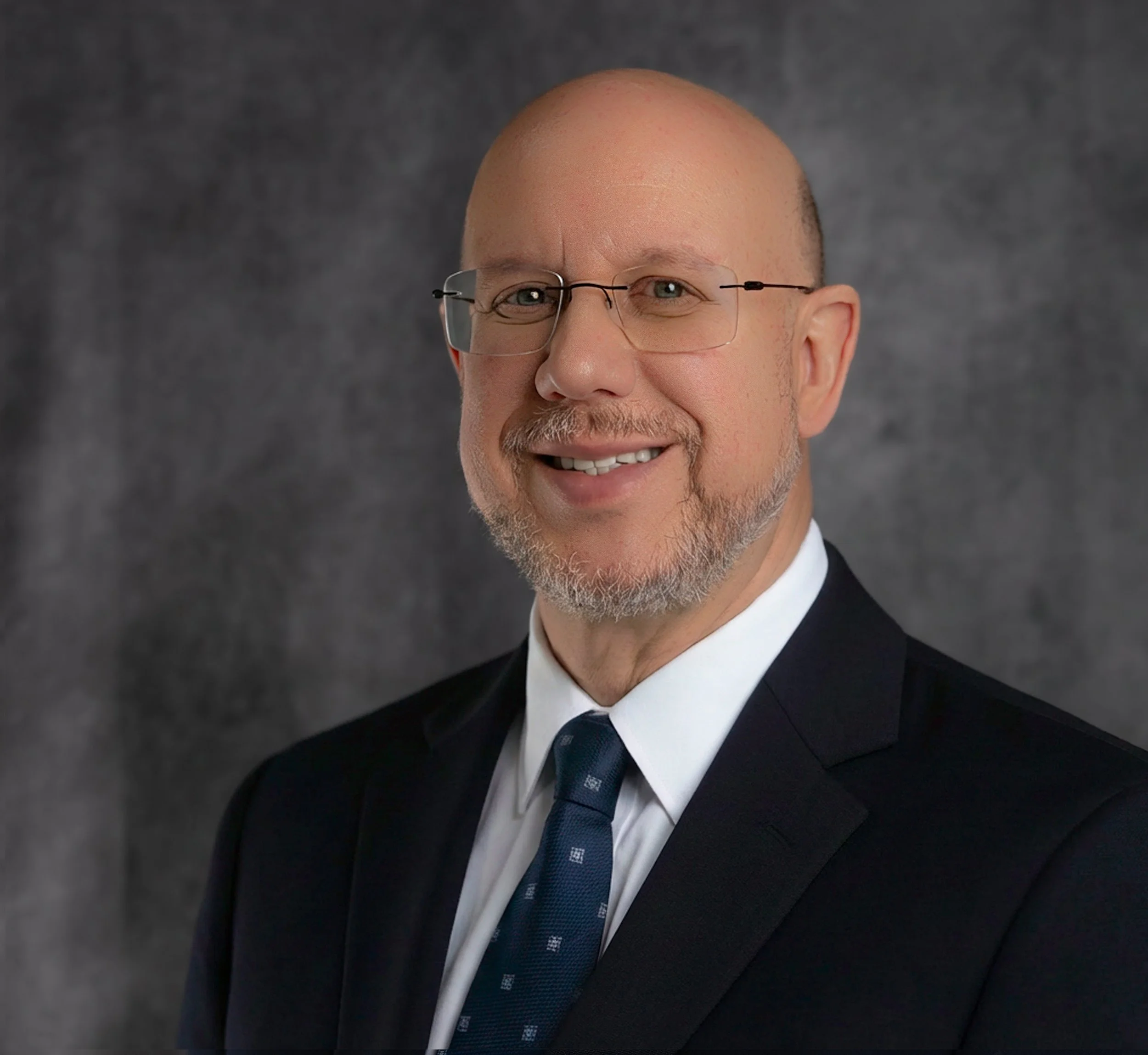 A young girl with blue eyes and blonde hair, wearing a tan floral dress with a belt, sitting amidst colorful fall flowers and pumpkins, holding a small orange pumpkin.