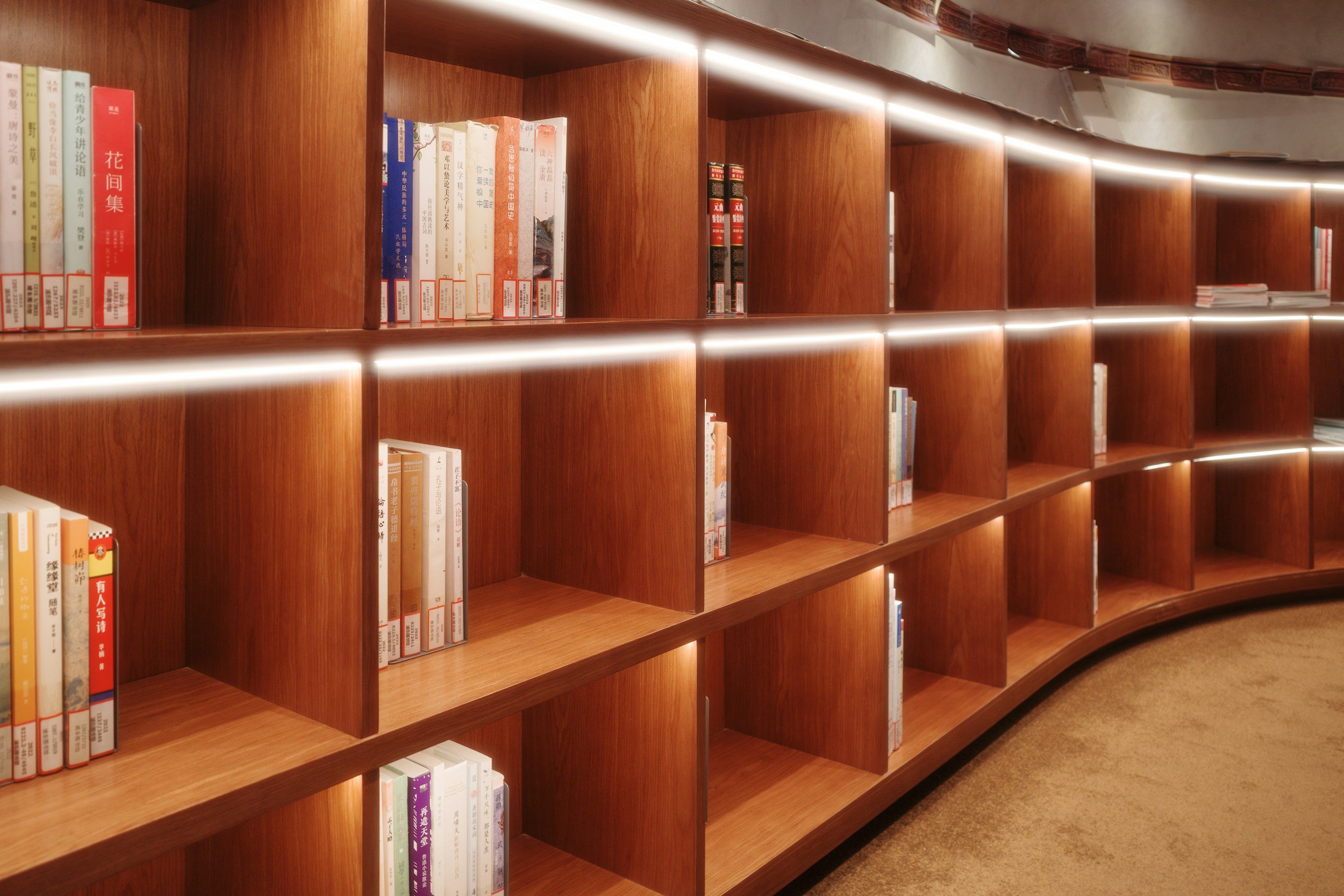 Estantería de madera curva con libros en una biblioteca, iluminada con luces integradas.