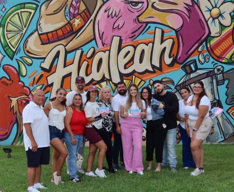 Group of people standing in front of a colorful mural with the text 'Hialeah', holding certificates or awards.