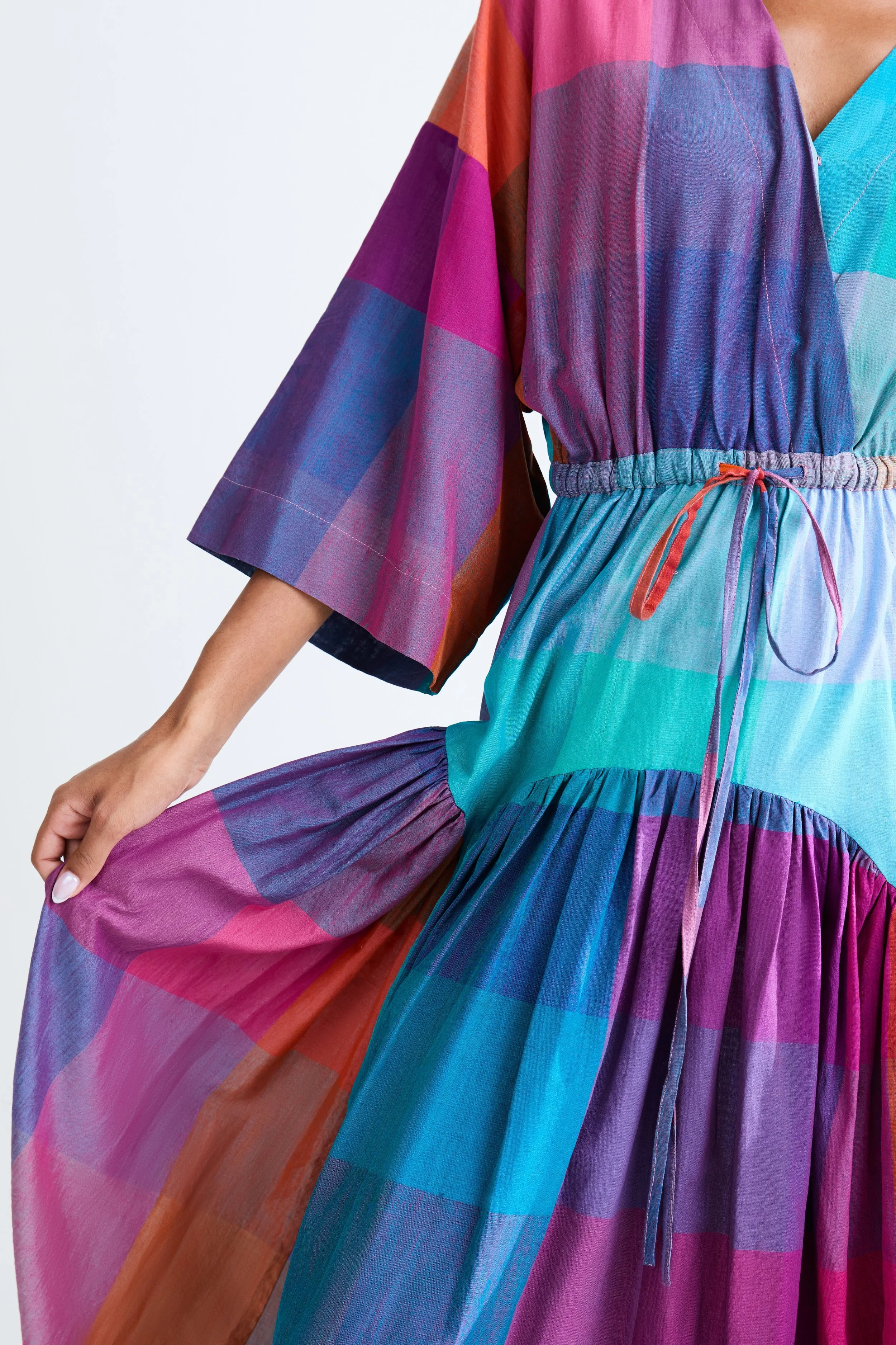 A colorful dress with a patchwork pattern in purple, pink, blue, green, and orange, featuring a drawstring waist and wide sleeves.
