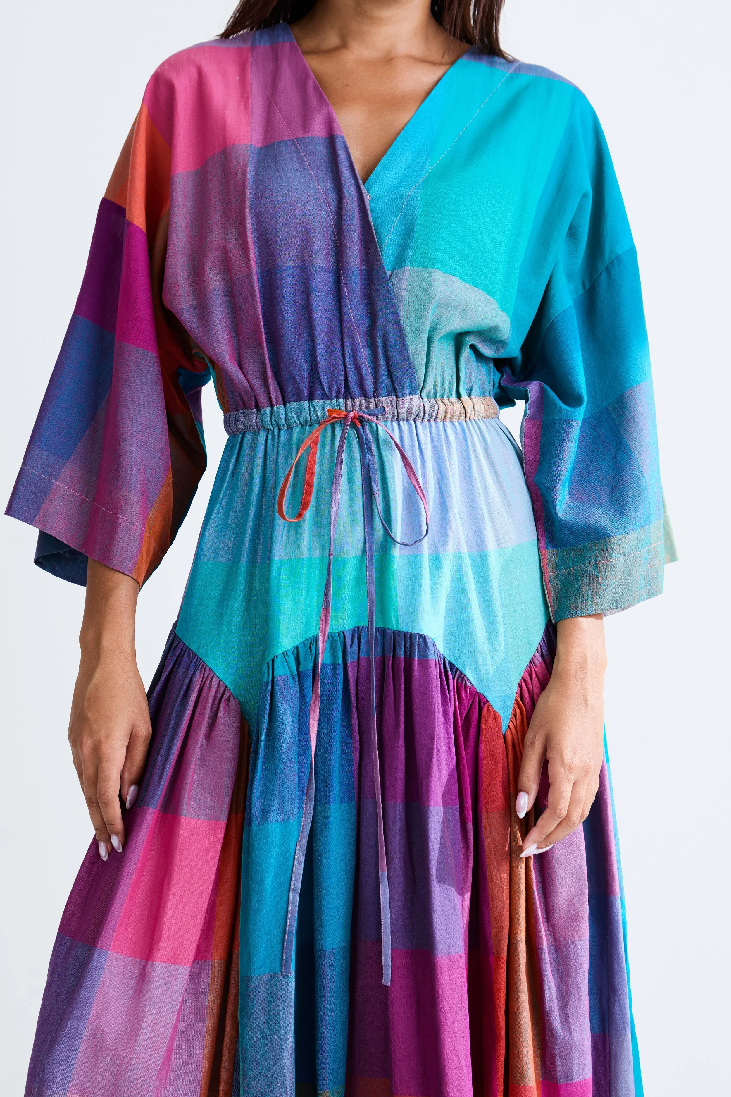 Woman wearing a colorful, patchwork-style dress with long sleeves and a knotted waist.