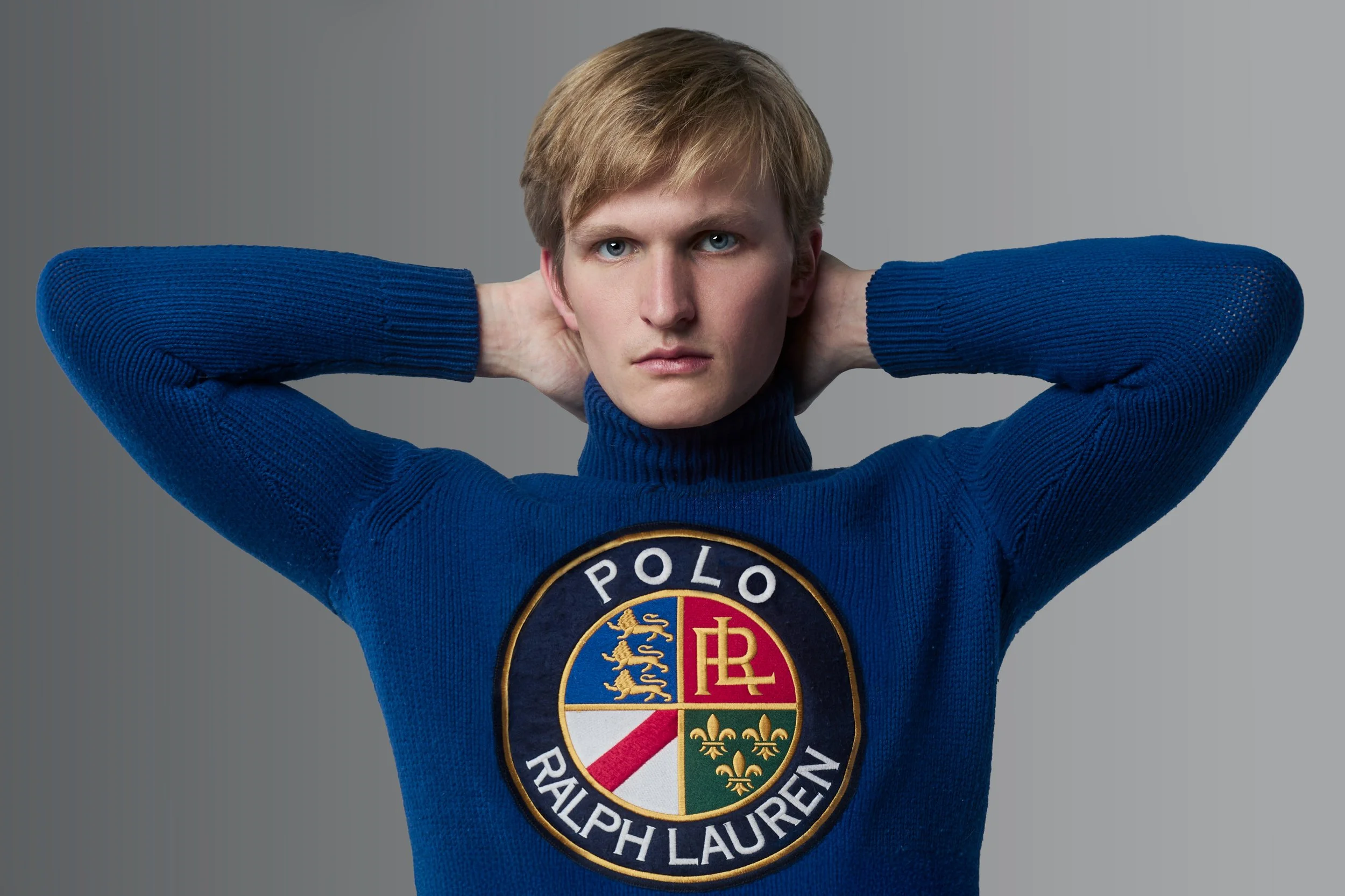 A young man with blond hair wearing a blue turtleneck sweater with the Polo Ralph Lauren logo