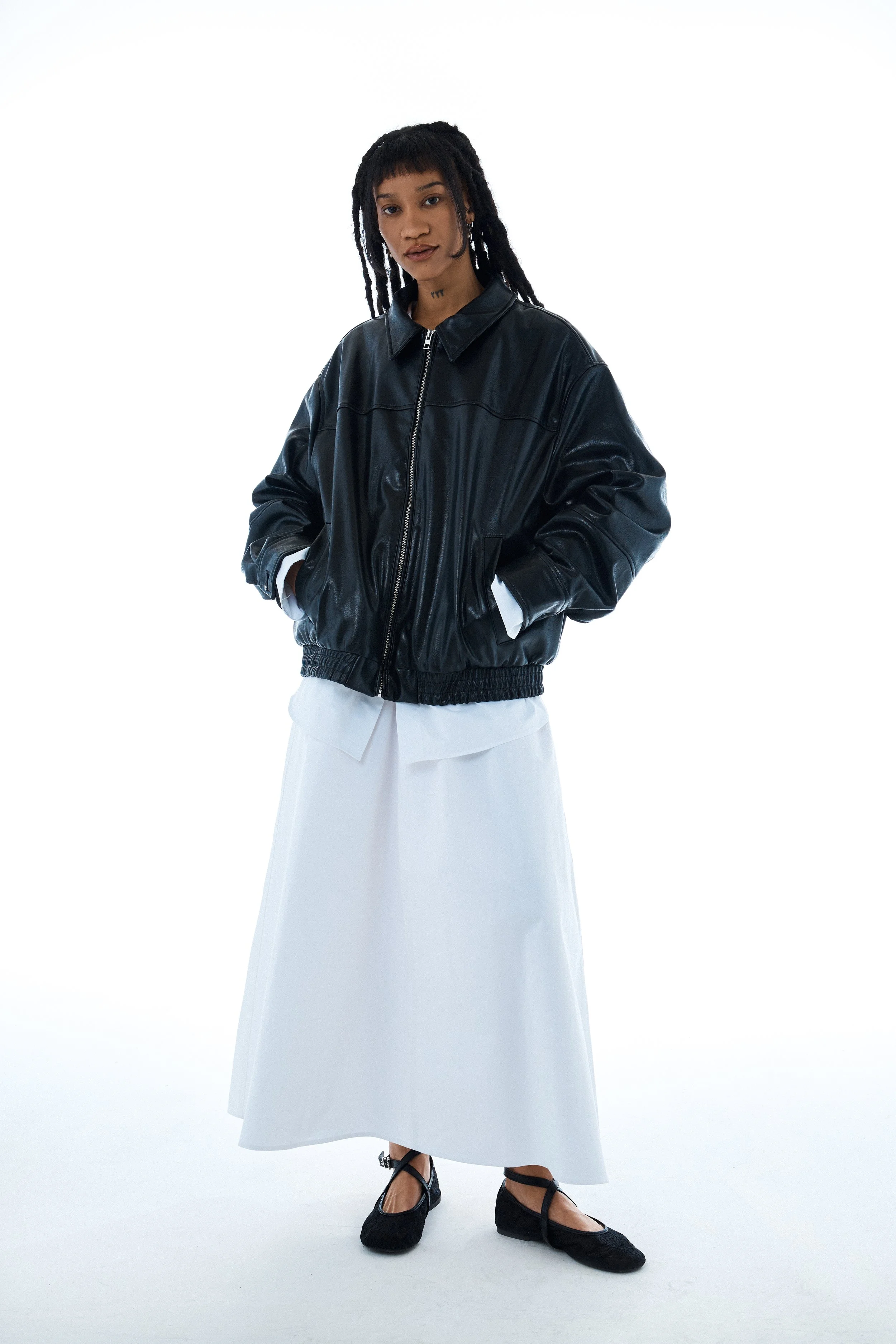 Fashion model wearing a black leather jacket, white skirt, and black shoes against a plain white background.