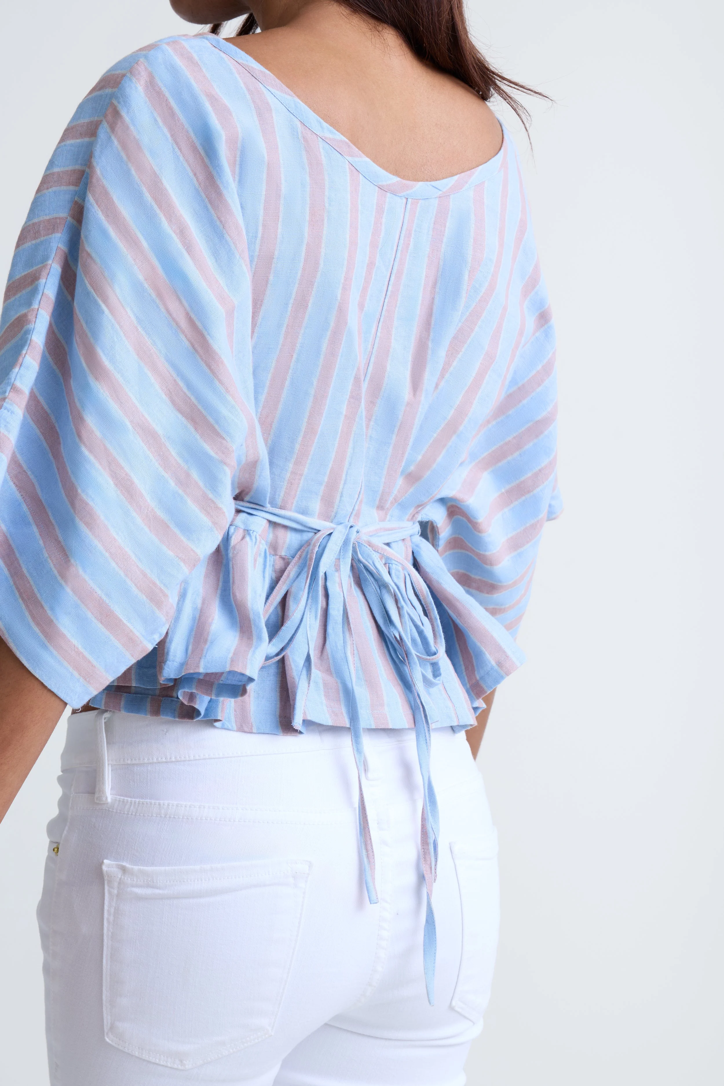 Woman wearing a light blue and pink striped blouse with a bow at the waist, and white pants.