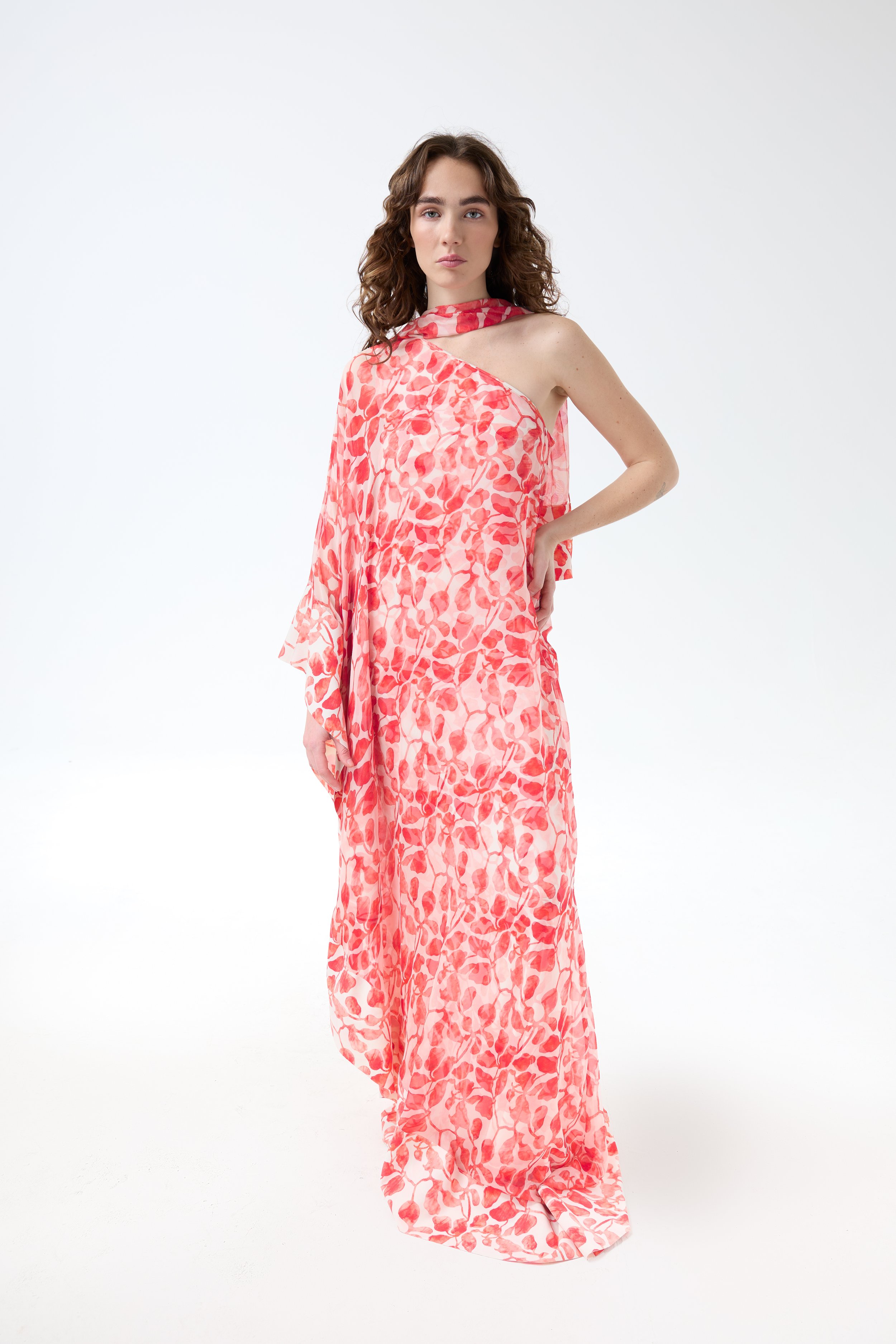 Woman wearing a long, flowing dress with a pink and red floral pattern, standing against a white background.